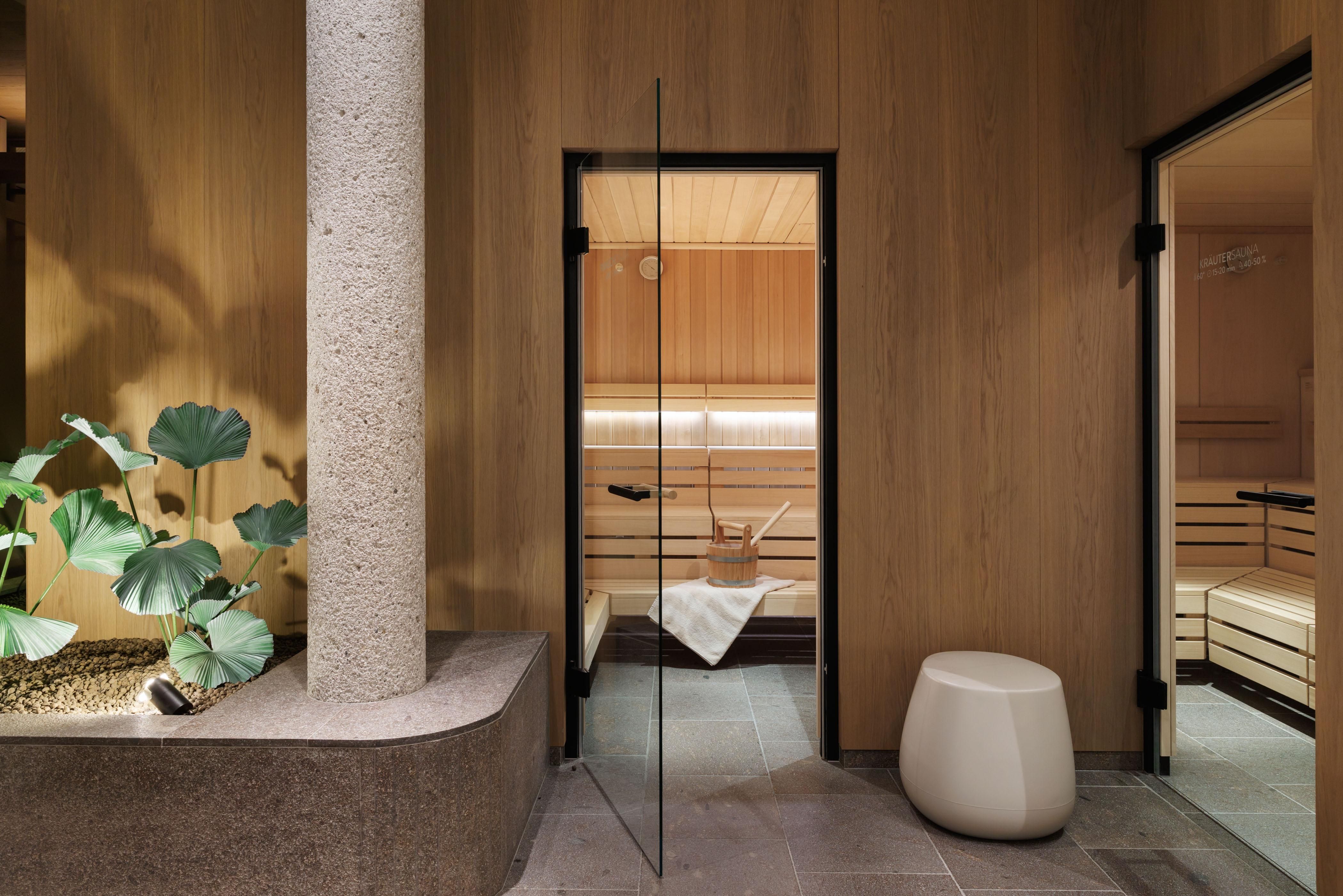 A modern wellness area with a sauna and a minimally designed room. A green plant arrangement and bright wood walls create a relaxing atmosphere.