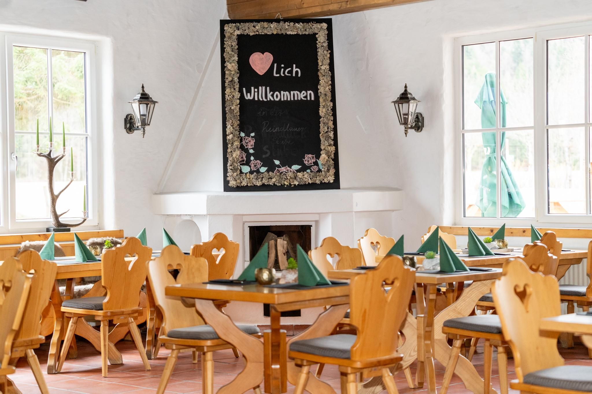 A bright, inviting restaurant with wooden tables and chairs. A welcome sign hangs on the wall in a friendly design.