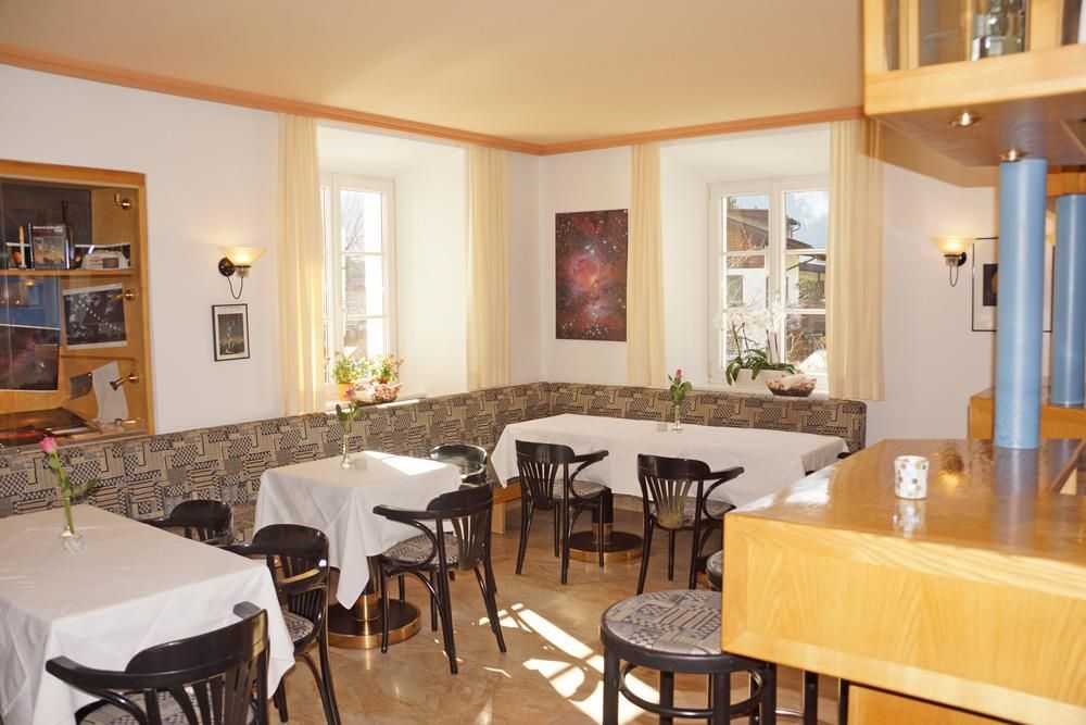A cozy room with tables and chairs. The walls are partially decorated with artworks, and there are fresh flowers on the tables.