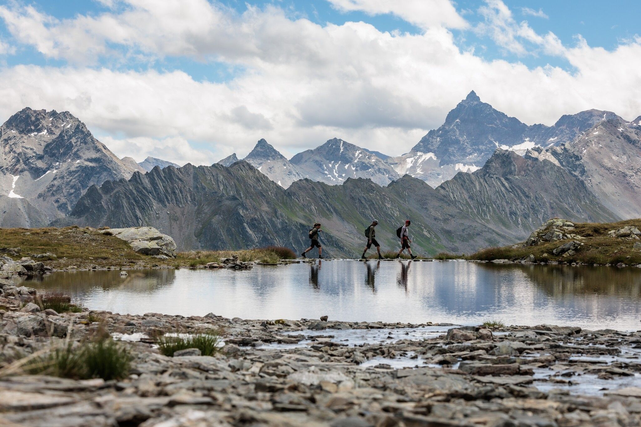 Auf der 6. Etappe am Paznauner Höhenweg. Wanderer am kleinen Bergsee mit schroffen Bergen im Hintergrund.