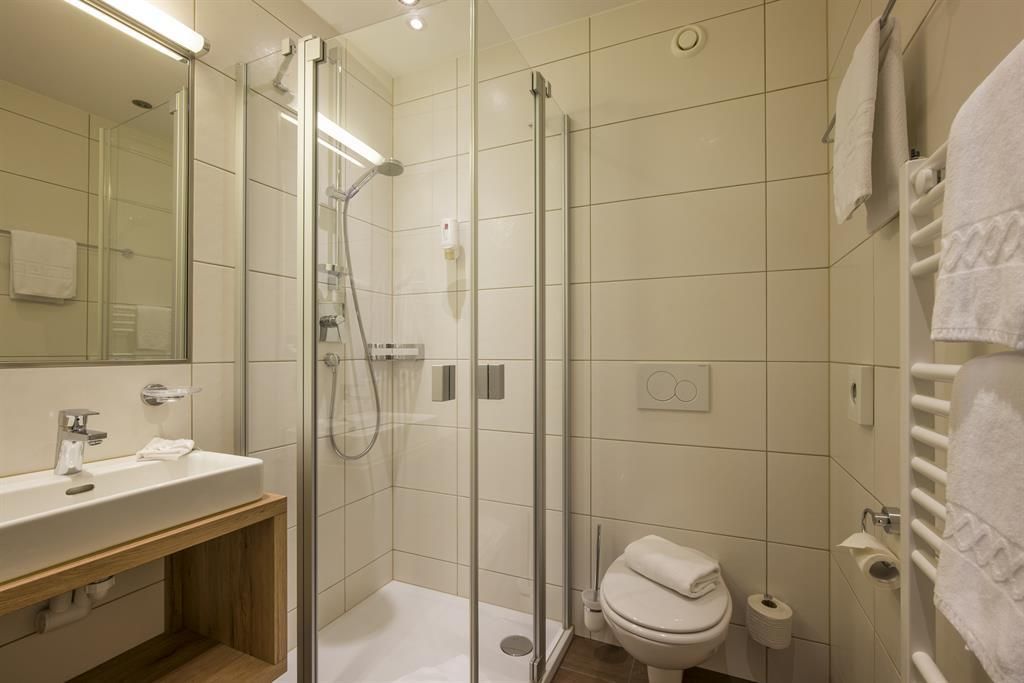 A modern bathroom with clean lines. It features a glass shower, a sink, and a toilet.