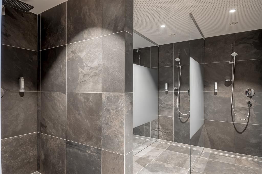 A modern shower with dark tiles and a clear glass wall. The room is well-lit and offers an elegant design.