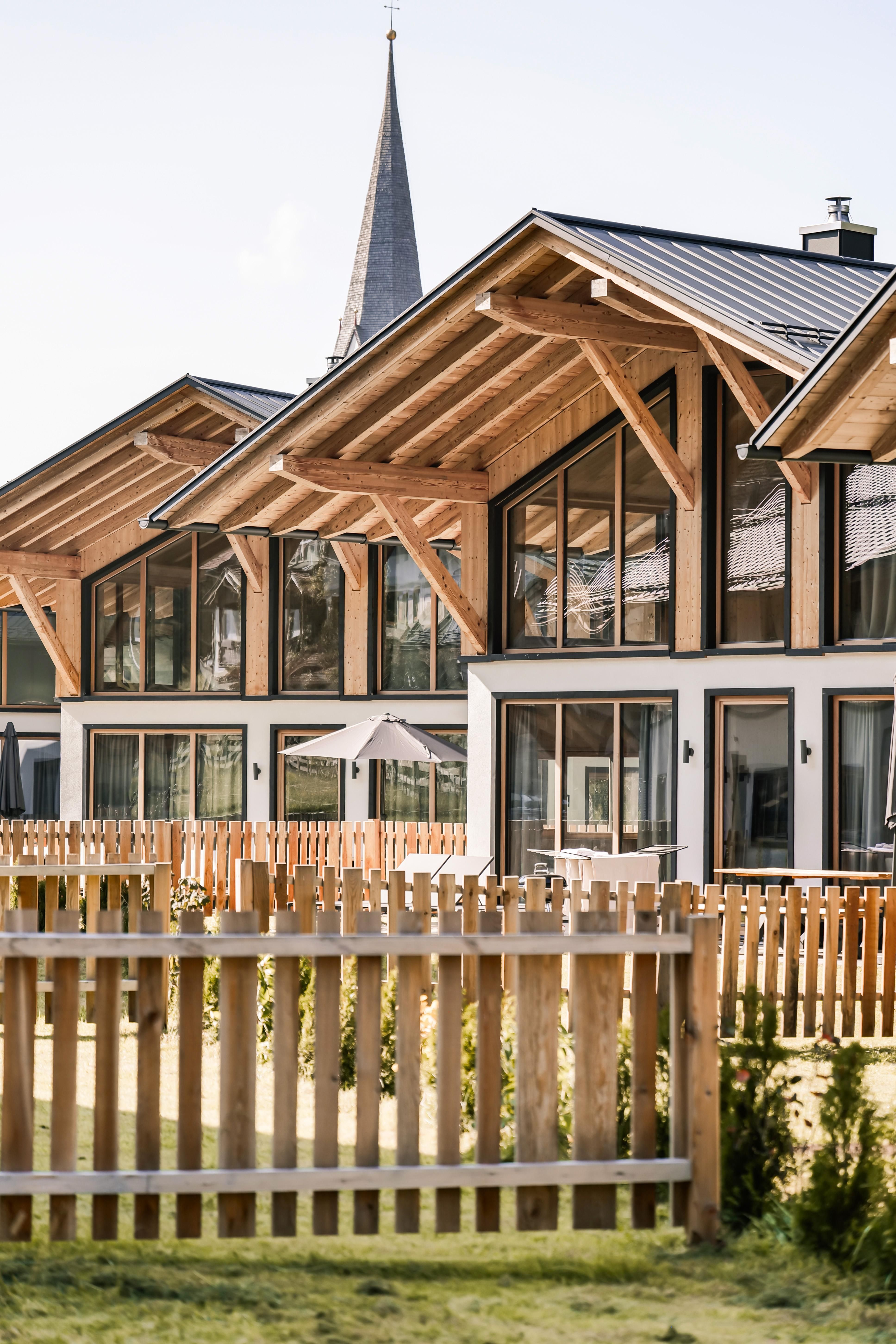 Modern wooden houses with large windows in a quiet residential area.
In the foreground, there is a lovely wooden fence and a well-maintained green space.