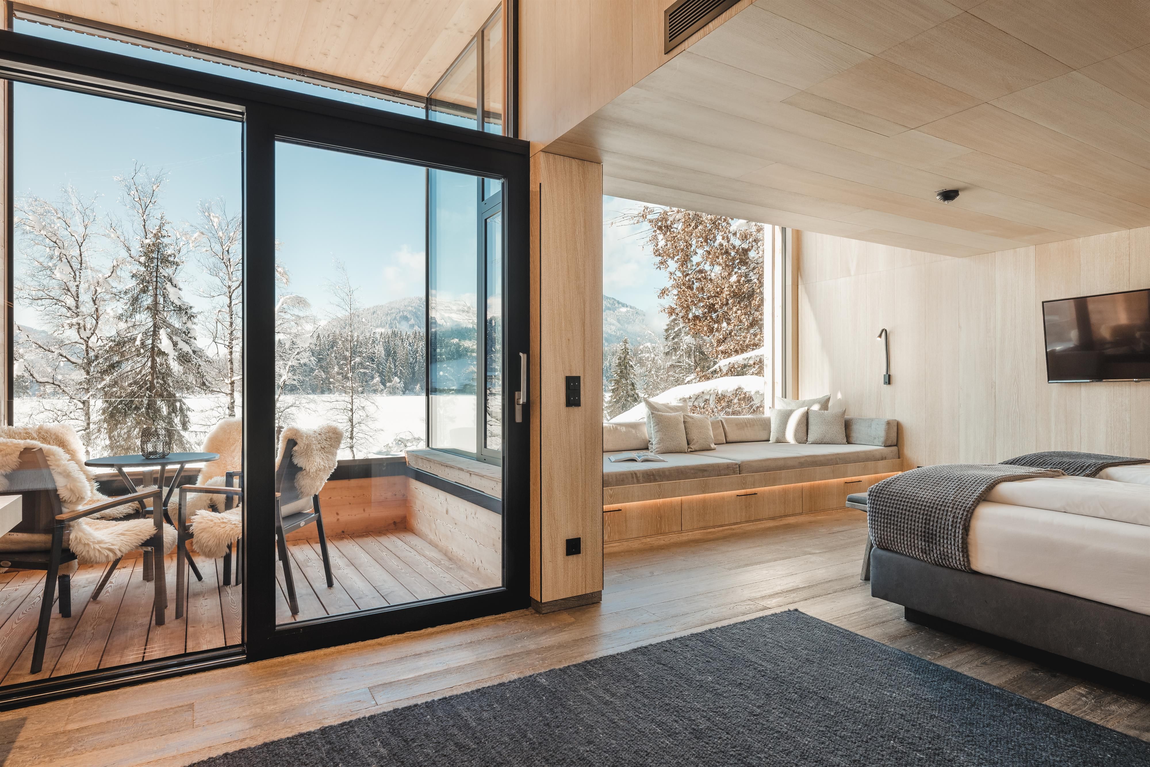 A modern room with wooden decor and large windows. Outside you can see a wintry mountain landscape.