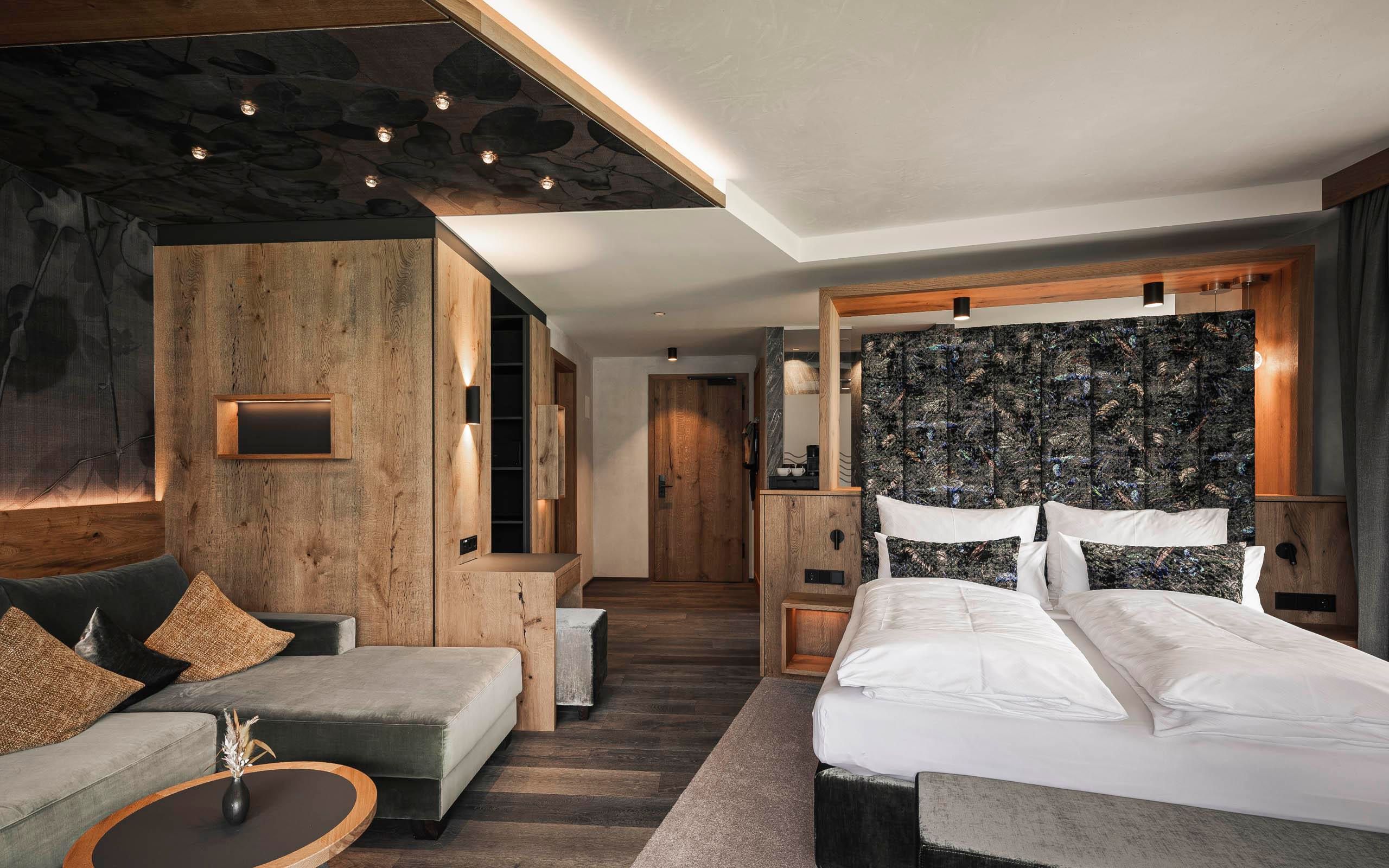 A modern hotel room with wooden paneling and a cozy sofa. There are two single beds and a stylish décor.