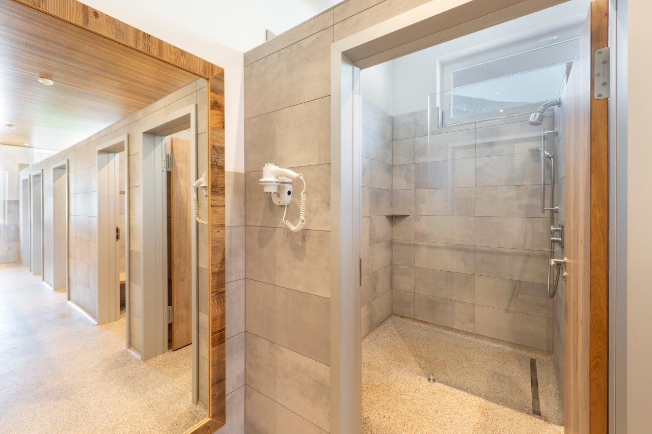 A modern bathroom with multiple shower cabins. The walls are designed with gray tiles and wooden paneling.