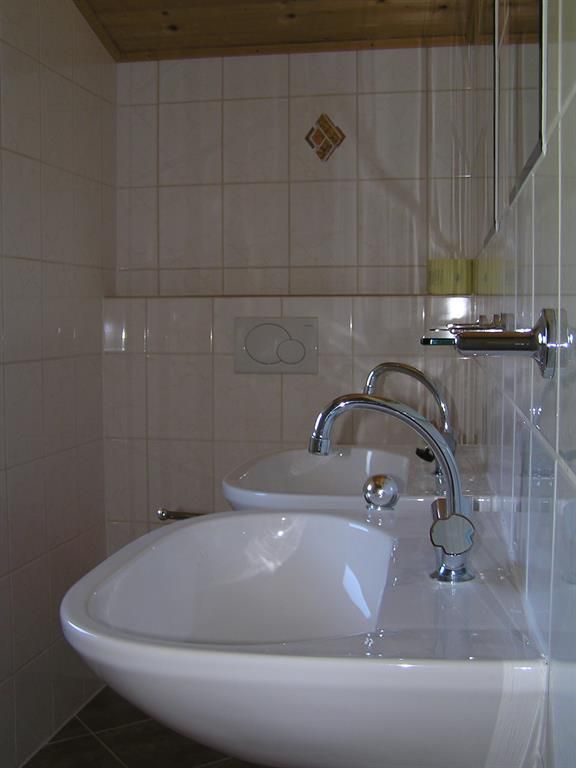 A modern bathroom with two sinks and elegant faucets. The walls are tiled and the furnishings are functional.