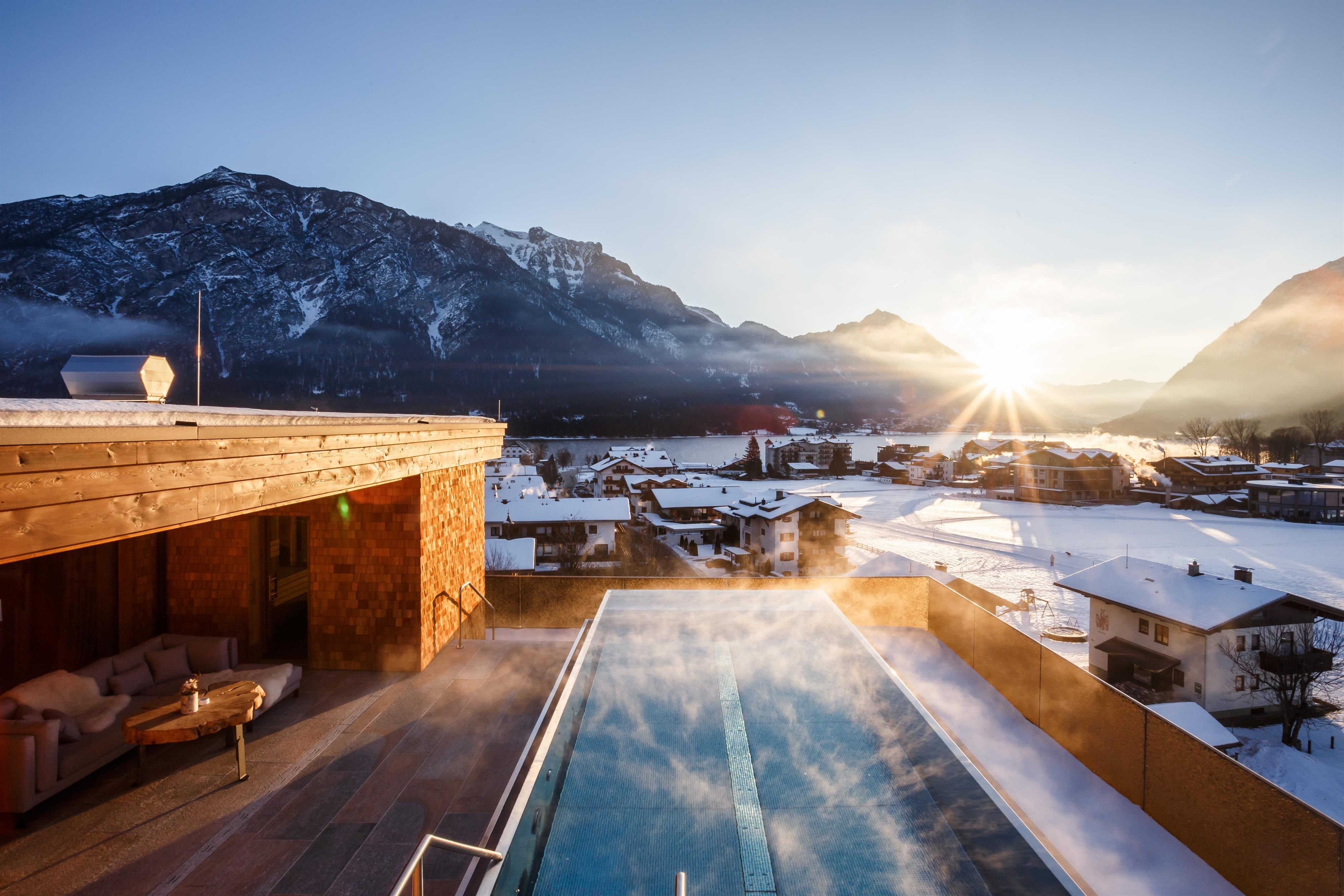 A view of a beautiful mountain panorama with a heated pool in the foreground. The sun is rising and bathing the snowy landscape in warm light.