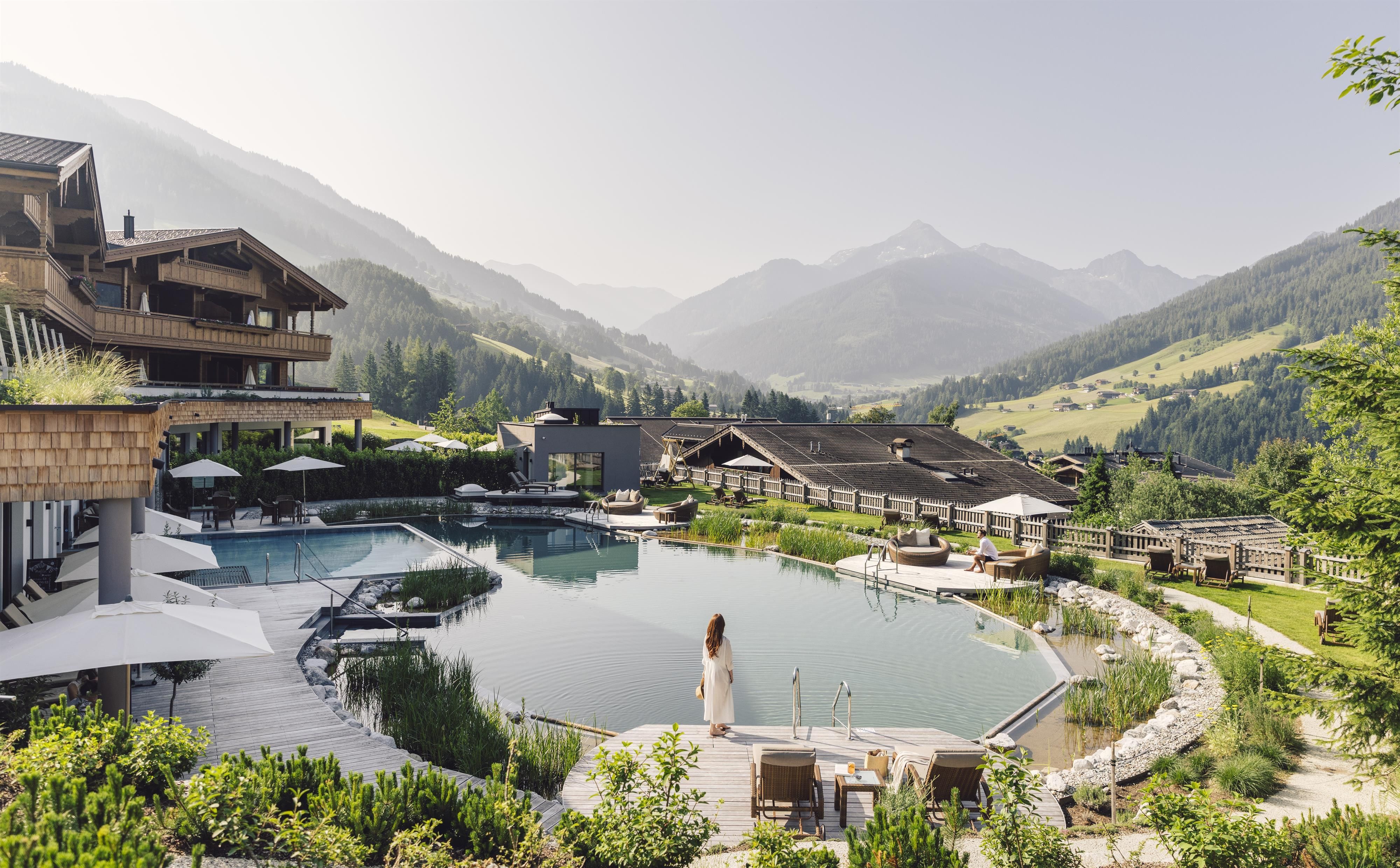 A beautiful resort in the mountains with a clear pool and a picturesque landscape. In the background, gentle hills and elegant buildings can be seen.