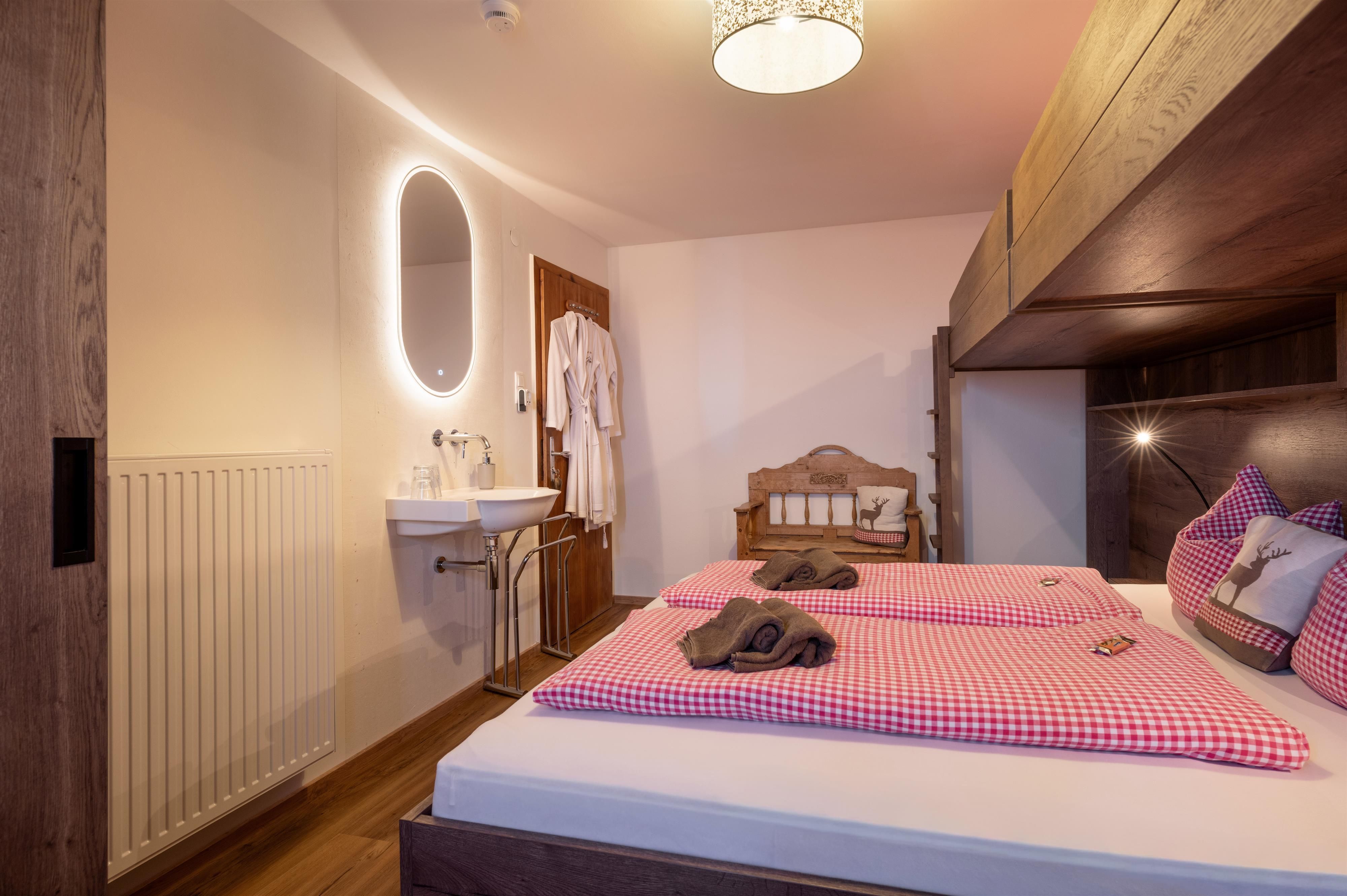 A modern bedroom with a double bed and checked pillows. The room is brightly and friendlily furnished, with a sink and a mirror on the wall.