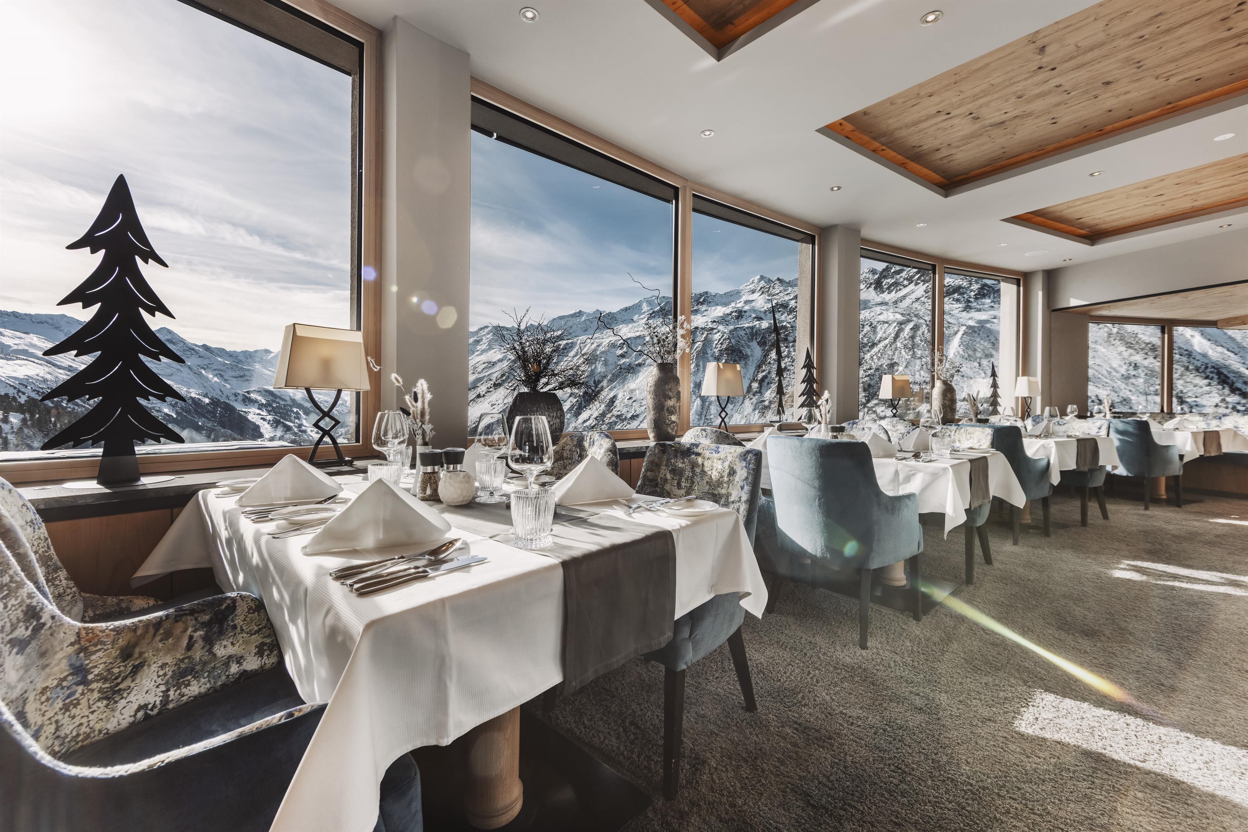 An elegant restaurant with large windows and a view of the snow-covered mountains. The tables are stylishly set, and the atmosphere is cozy.