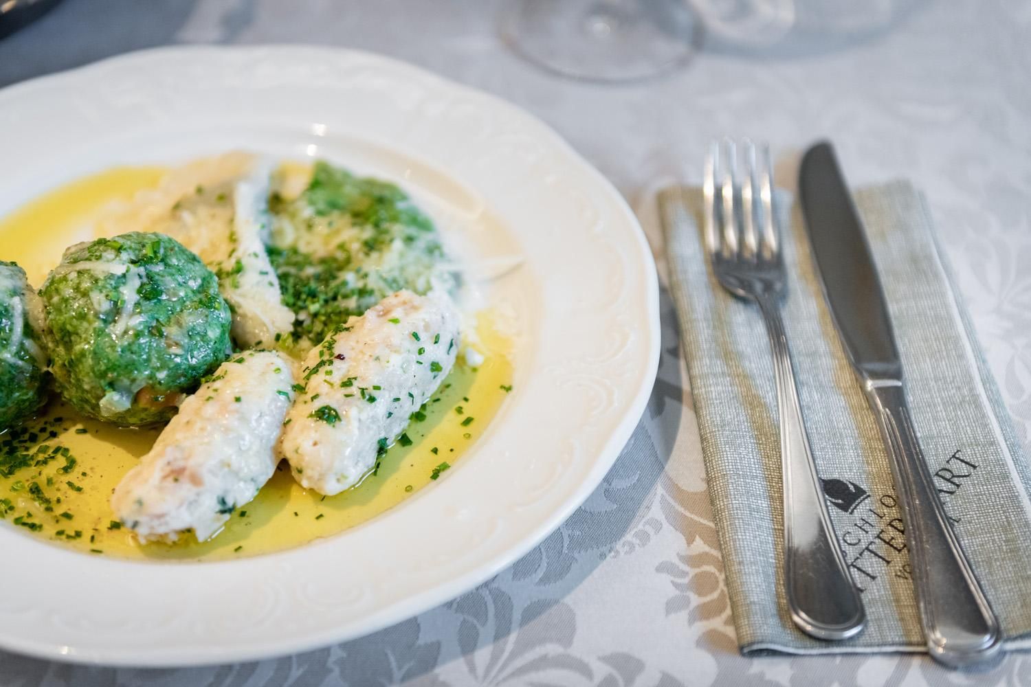 A plate with delicate fish dumplings and green herb dumplings in a creamy sauce. Fresh chives are sprinkled on top and the dish is elegantly set.