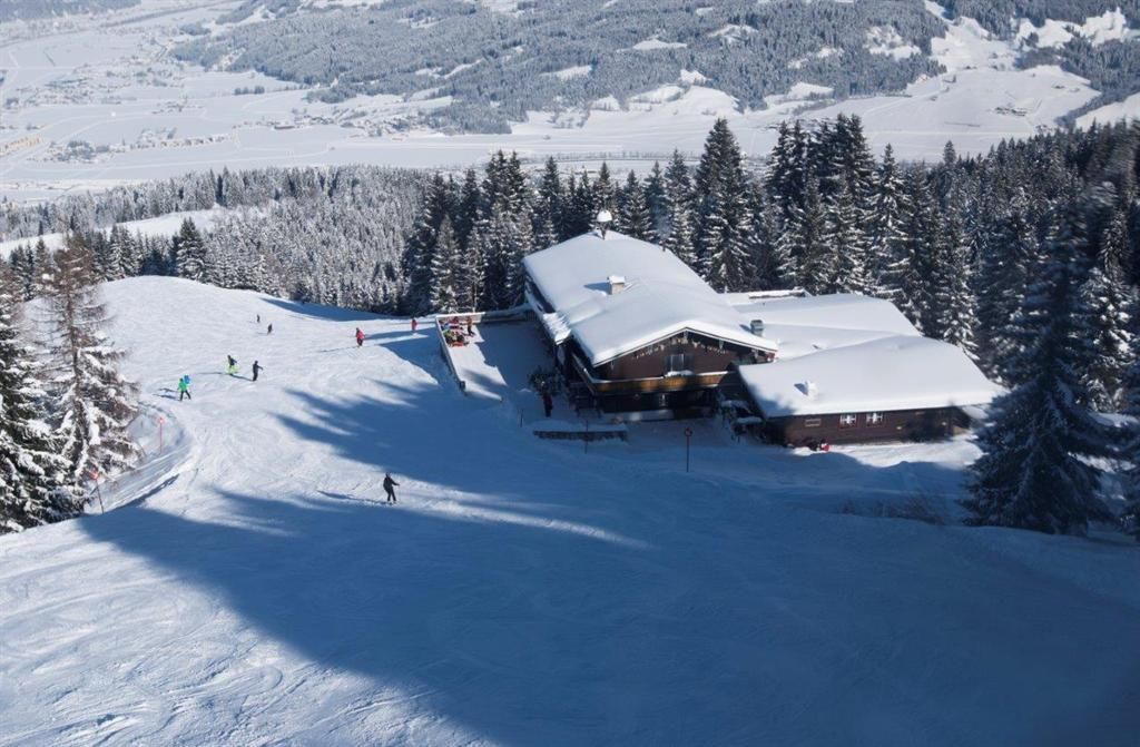 A snowy mountain landscape with a chalet and skiers. The trees are covered with snow and the sky is clear.