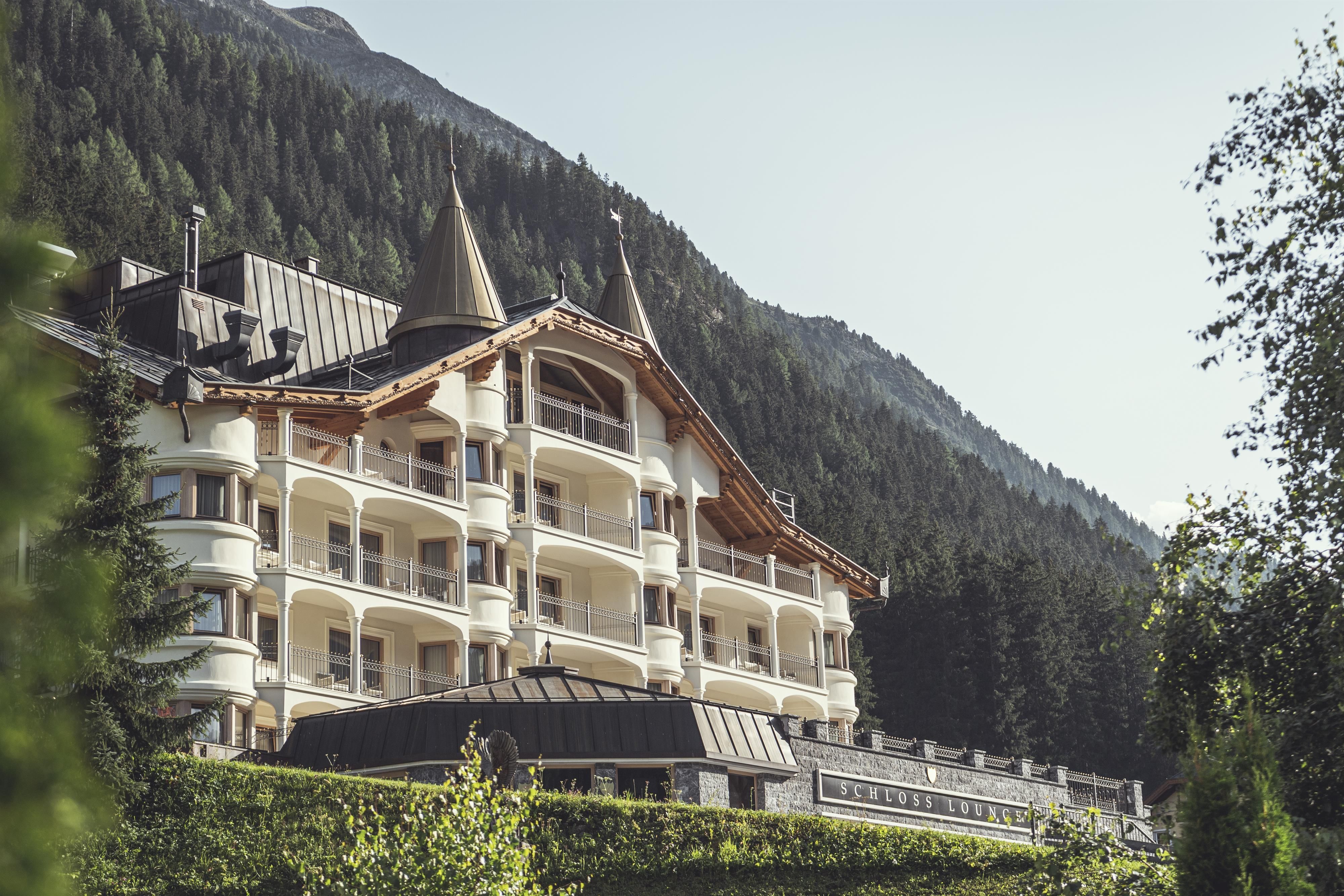 An elegant hotel in the mountains with pointed roofs and large windows. Surrounded by green trees and picturesque rocks.