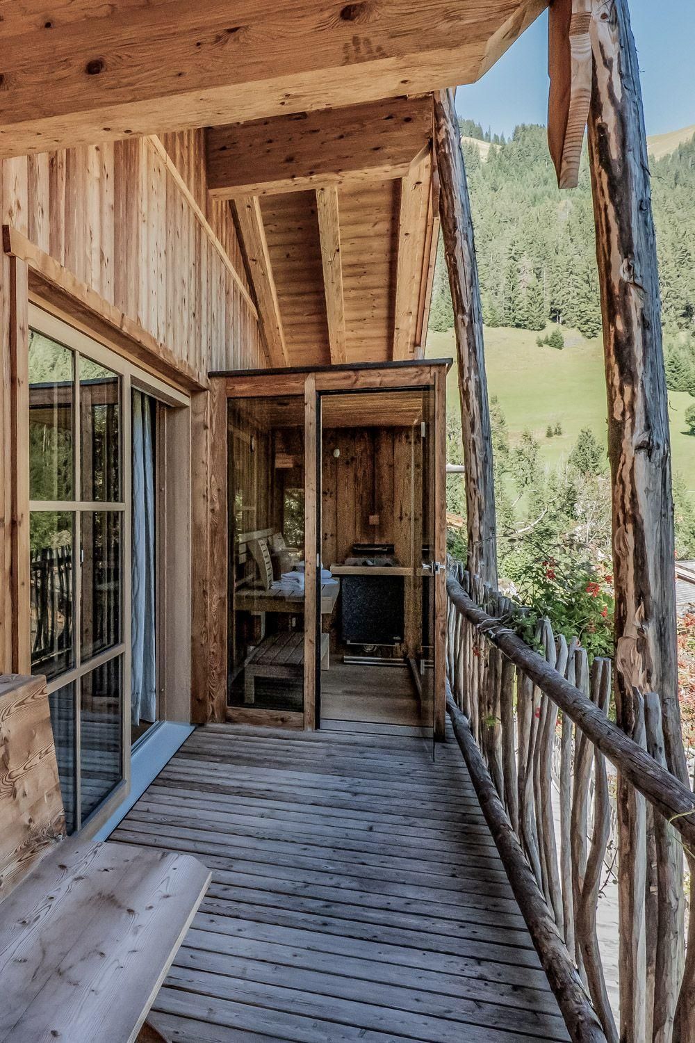 A cozy wooden balcony with a beautiful view of the green landscape. The balcony is equipped with a small table and chairs and a sauna.