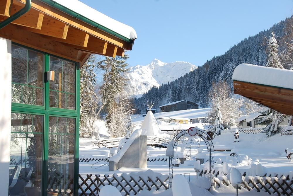 A snowy landscape with mountains in the background. The sun is shining on a chalet and the surrounding winter scenery.