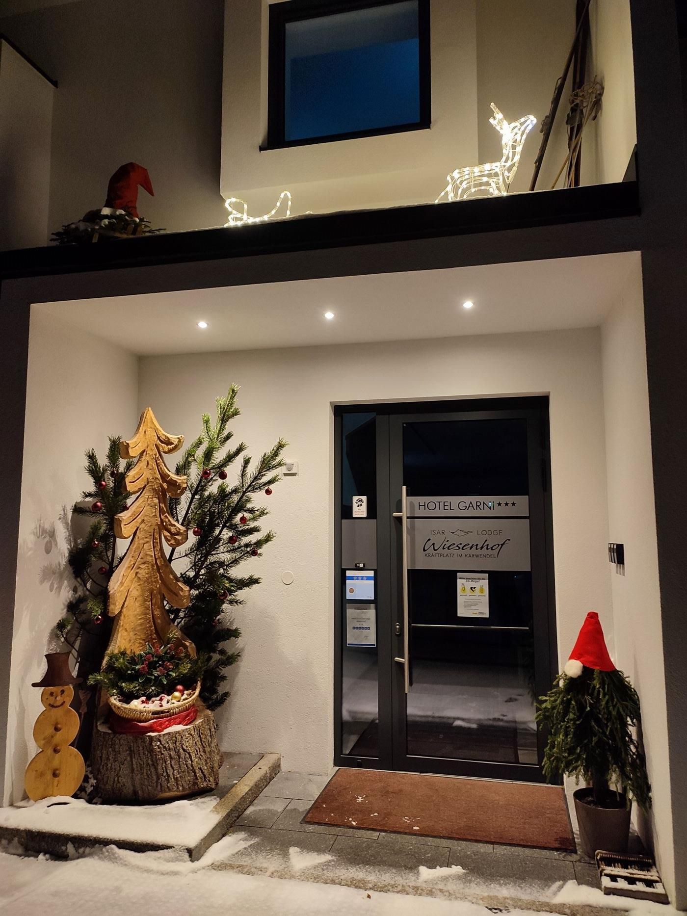 A festively decorated entrance with a Christmas tree and a snowman. The lights shine in the night, creating an inviting atmosphere.