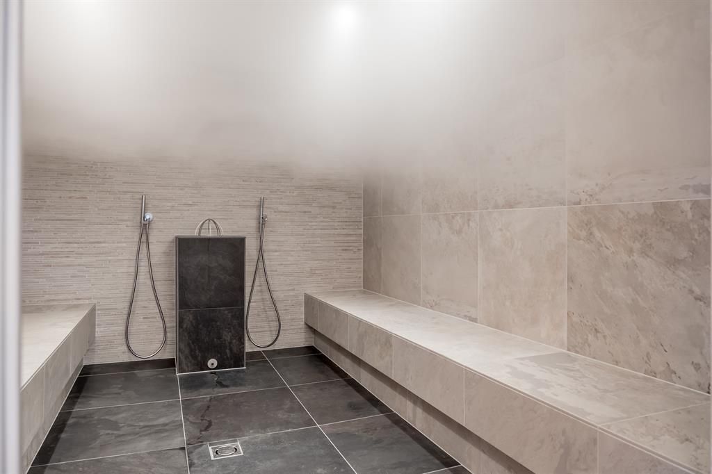 A modern steam room with bright tiles and two shower stations. The space is dimly lit and conveys a relaxing atmosphere.