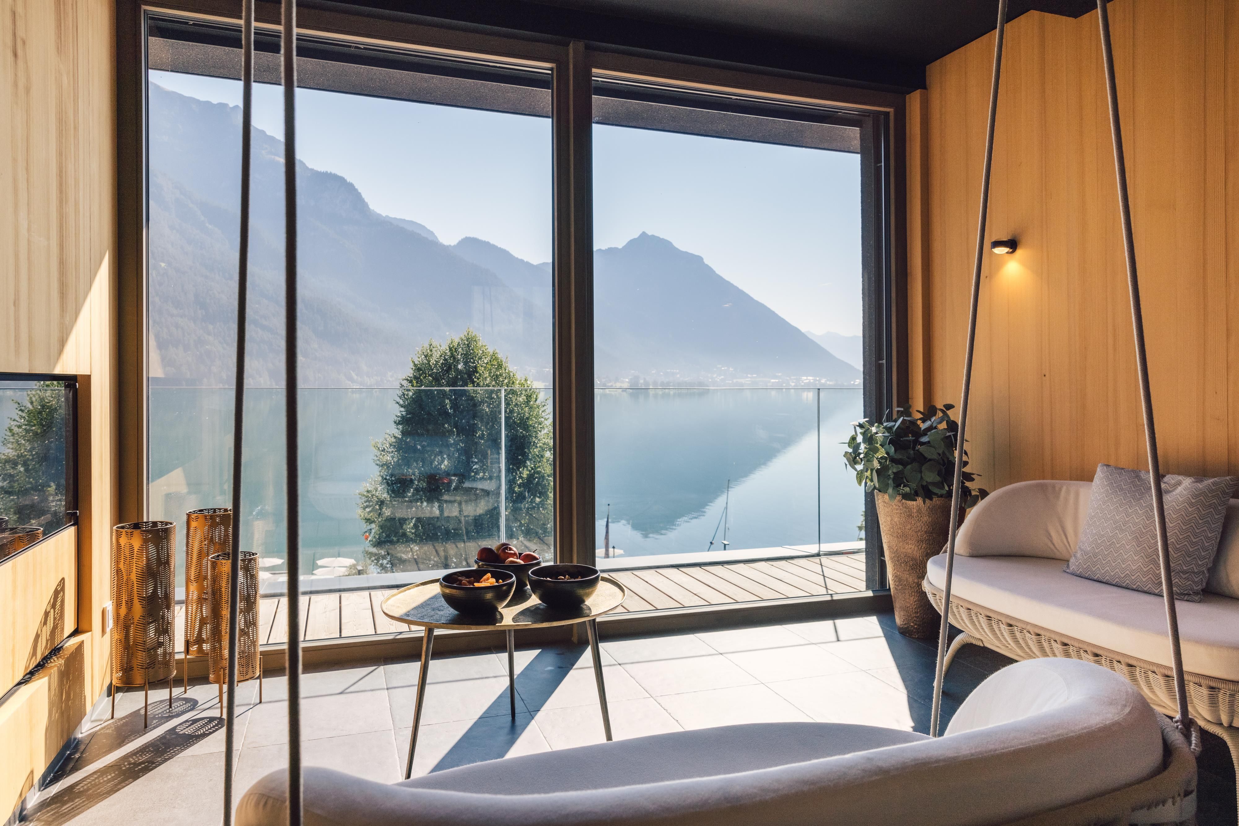 A modern living room with large windows that offer a stunning view of the lake and the mountains. The space is stylishly furnished and exudes tranquility and elegance.