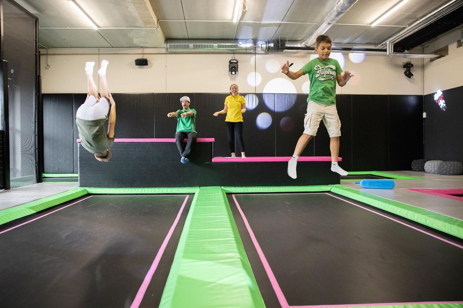 A trampoline park with several children jumping and doing tricks. The environment is colorful and inviting with trampolines in various colors.