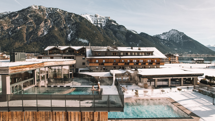 A luxurious hotel with a warm outdoor pool area in the snow. The impressive mountains create a picturesque backdrop.