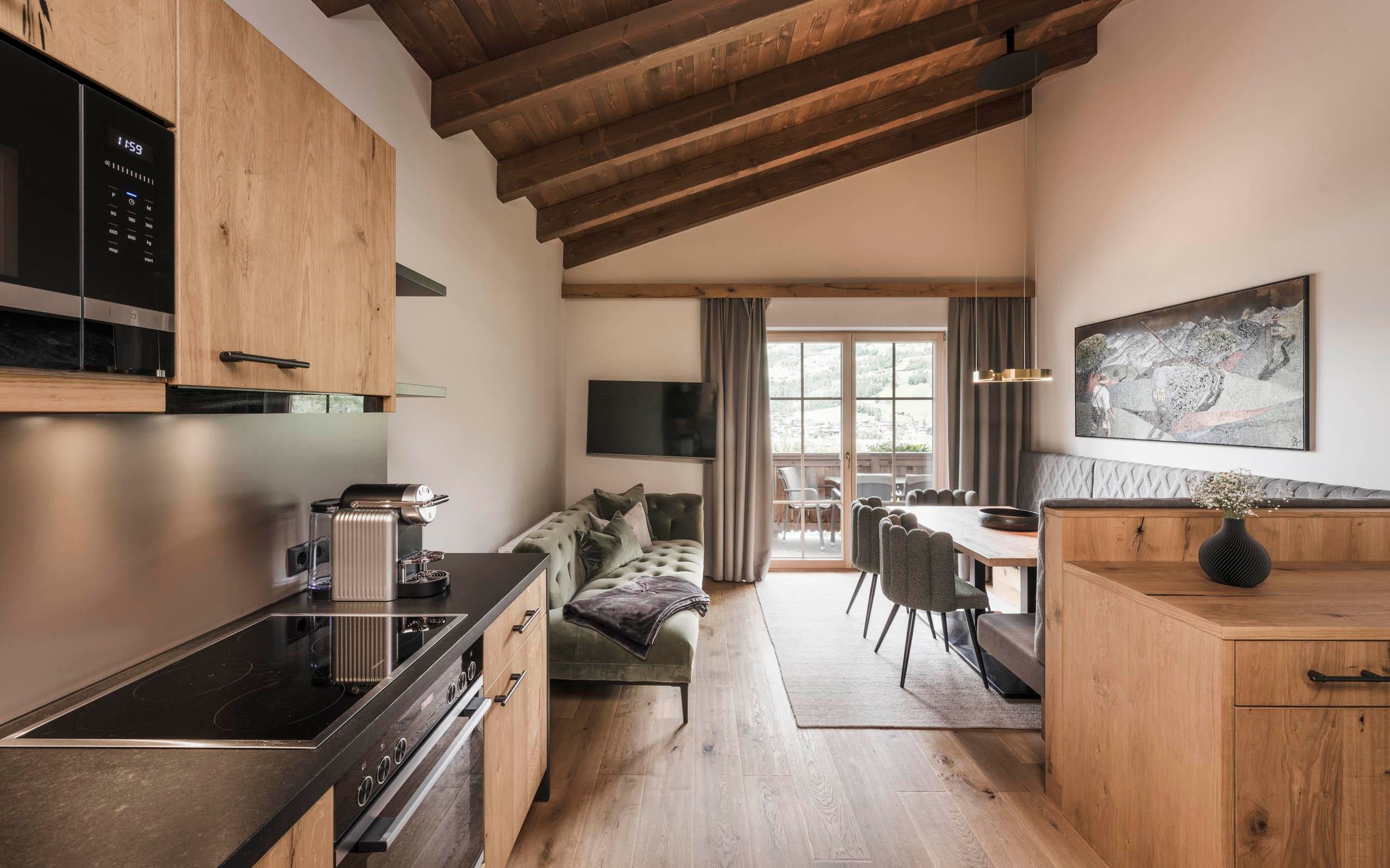 A modern kitchen with wooden furniture and an open living area. Large windows bring in plenty of light and provide access to a balcony.