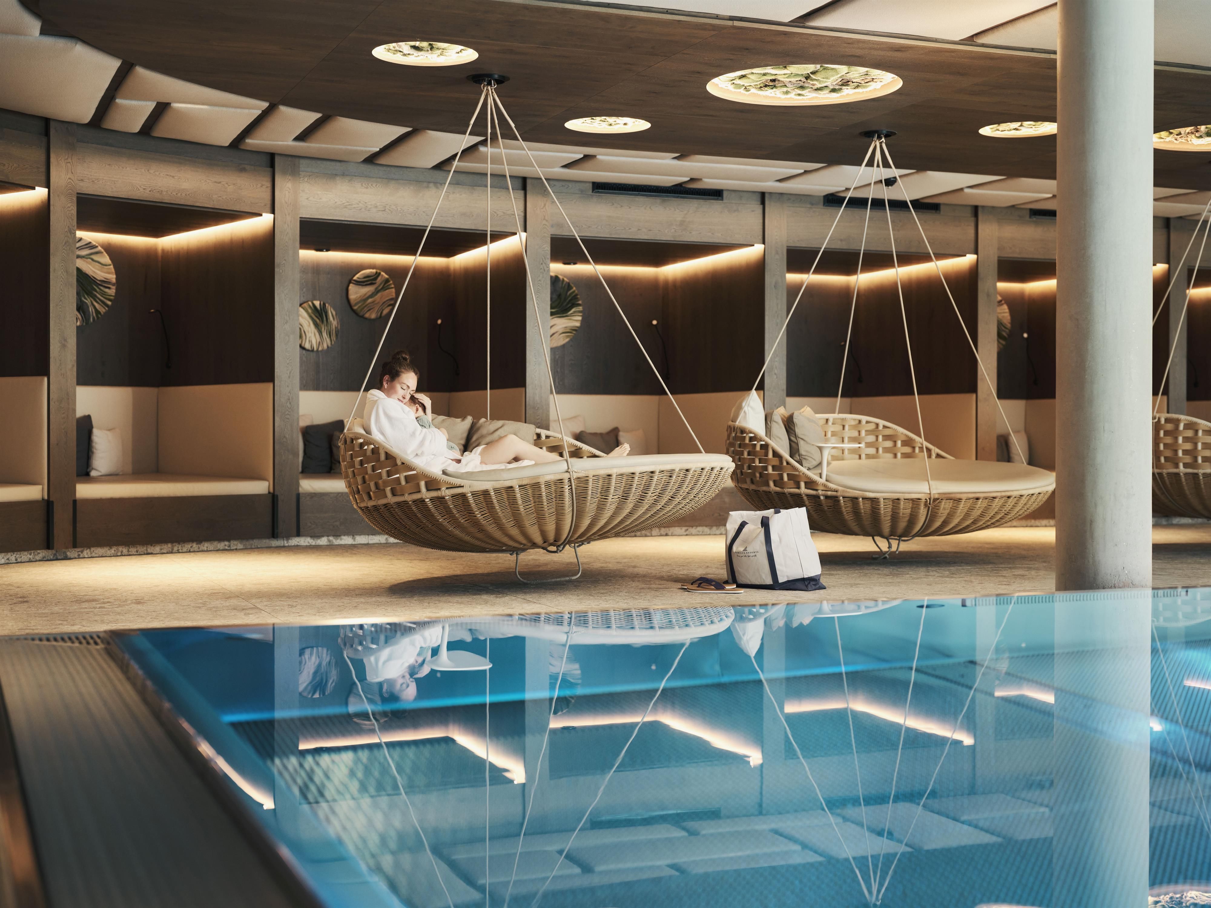 A modern spa with two hanging loungers and an open pool. Soft lighting creates a relaxing atmosphere.