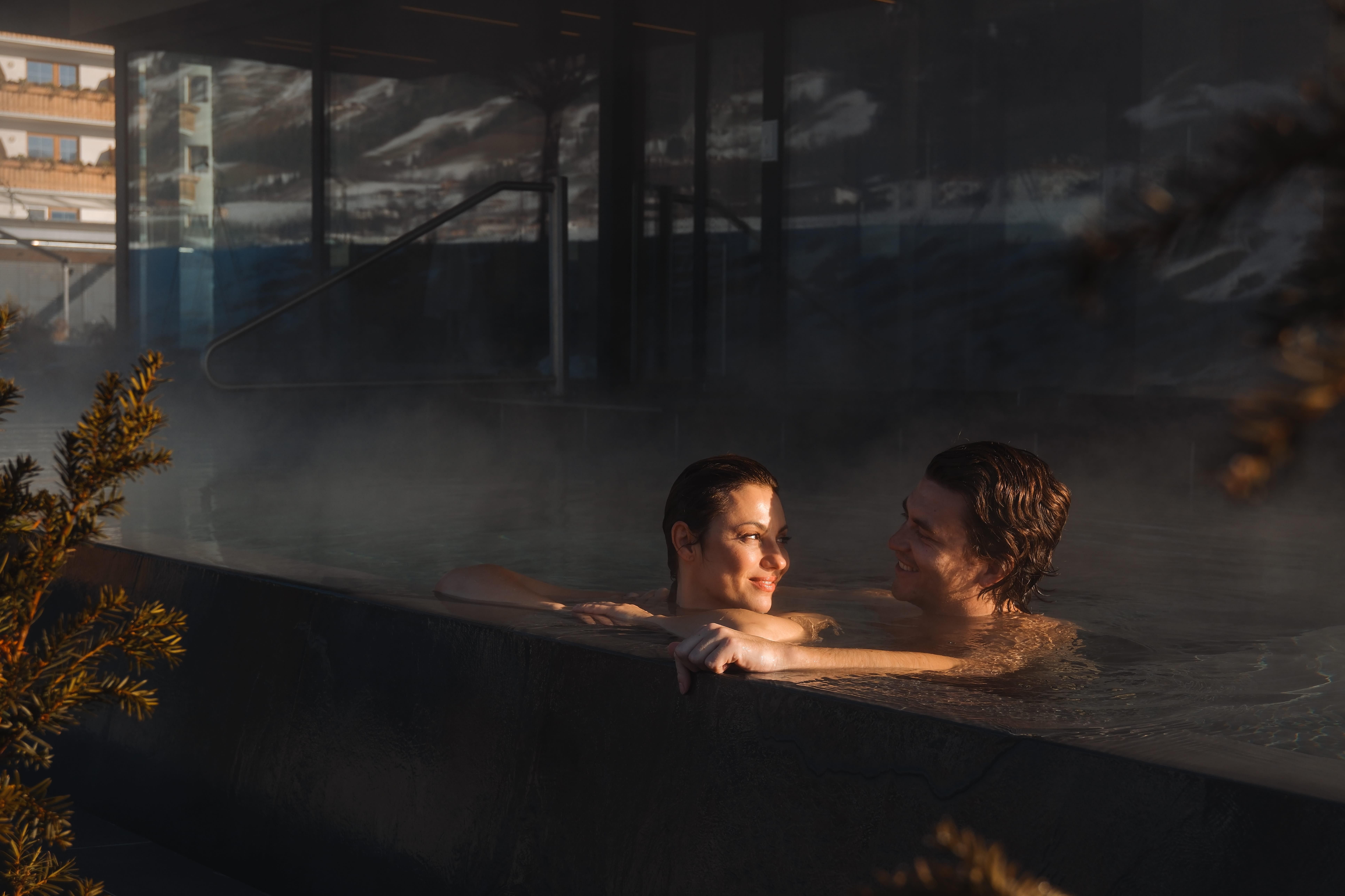 A couple relaxes in a steaming outdoor pool. The atmosphere is romantic and relaxing.