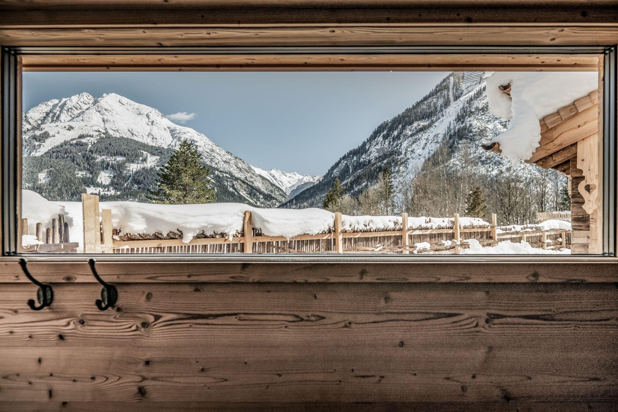 A view from a wooden window onto snow-covered mountains. The landscape is calm and wintry.