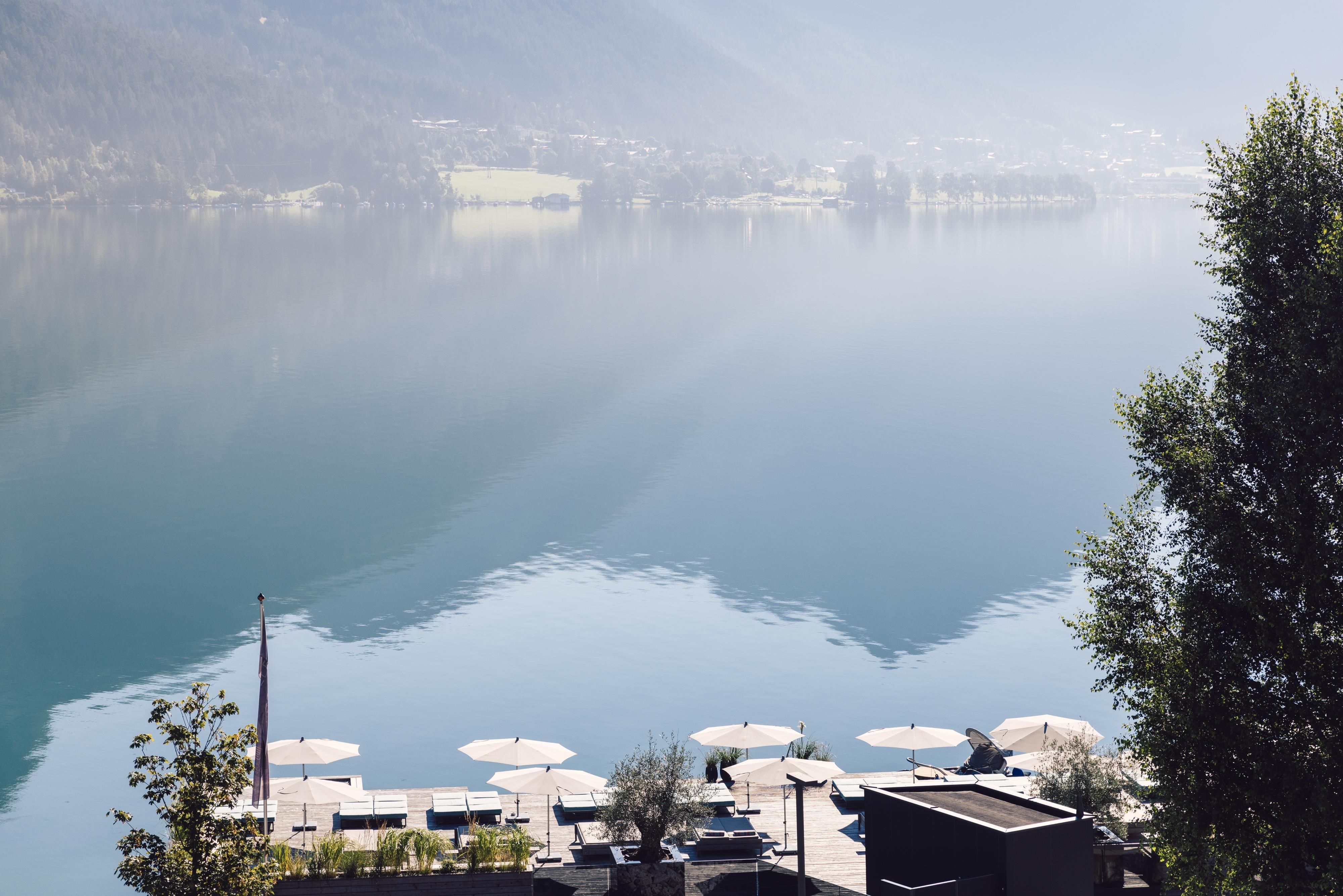 A quiet lakeside landscape with gentle mountains in the background. Relaxing loungers and sun umbrellas at the shore of the lake.