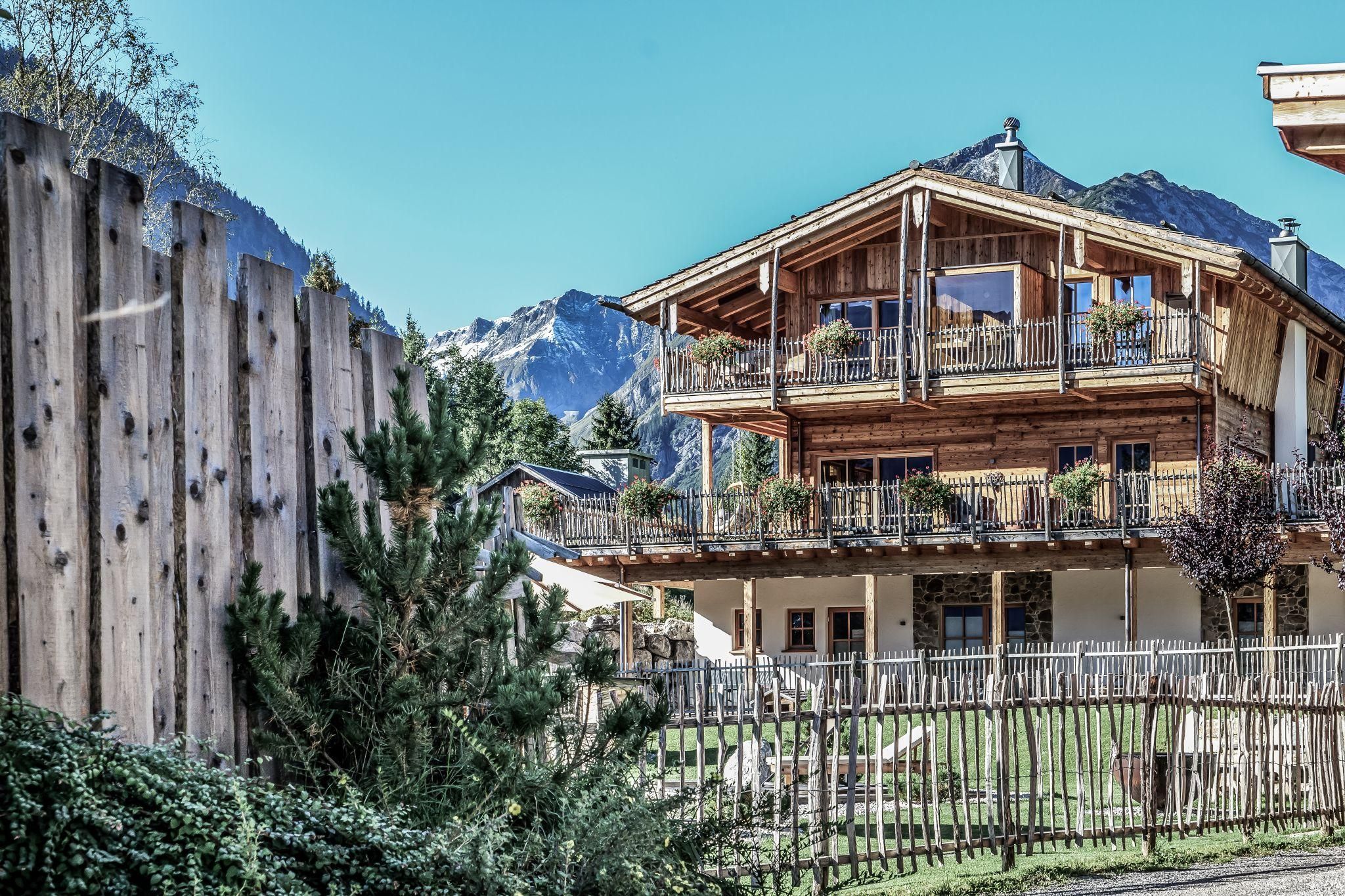 A charming chalet in the mountains with balconies and a beautiful view. In the foreground, you can see a fence and green grass.