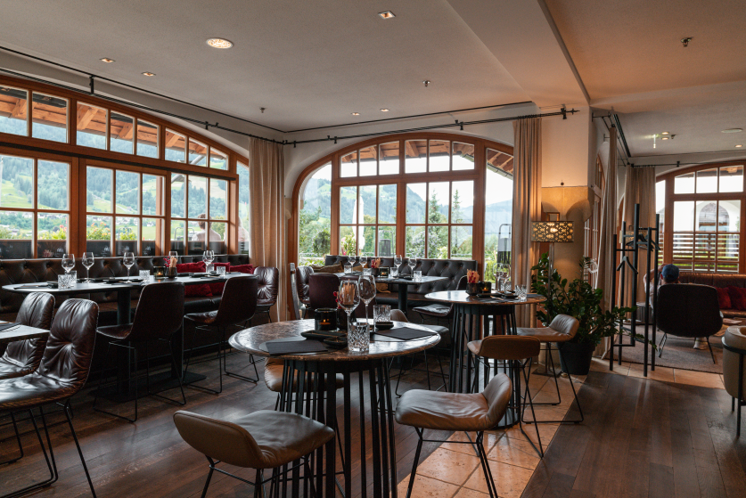 A stylish restaurant with circular seating and large windows that offer a view of the surrounding mountains. The decor is modern and inviting.