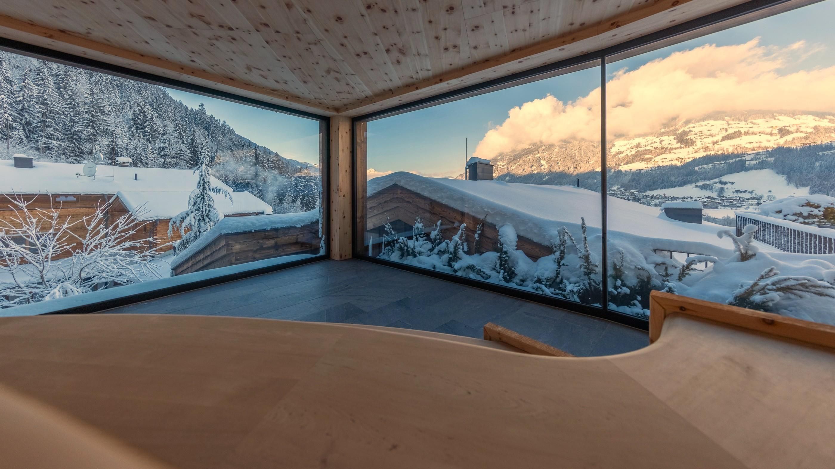 A modern room with large windows offers a view of a snowy landscape. The mountains and houses are hidden under a white blanket of snow.