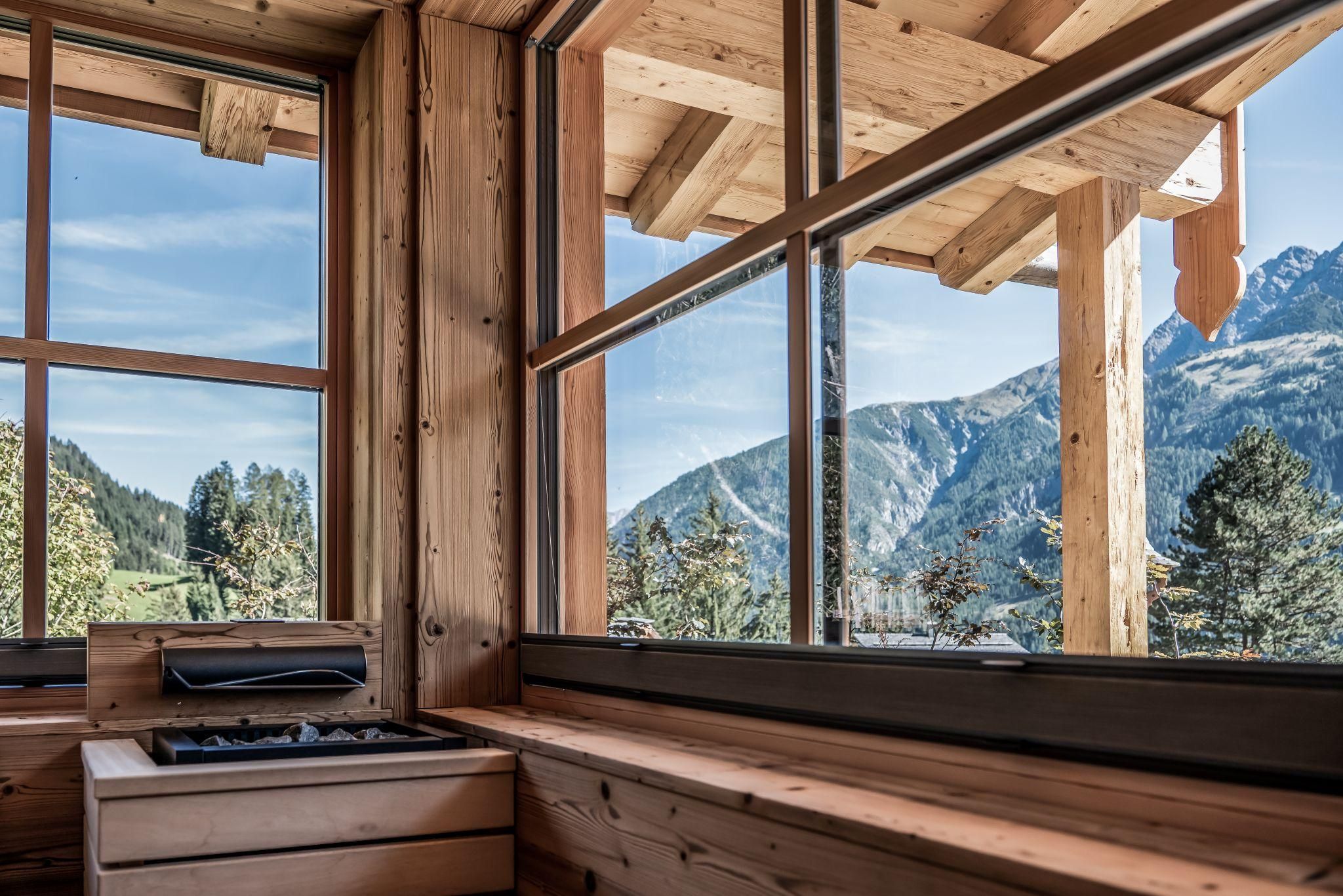 A cozy room with large windows that offers a view of majestic mountains and a clear sky. The wooden paneling adds a warm, natural atmosphere.