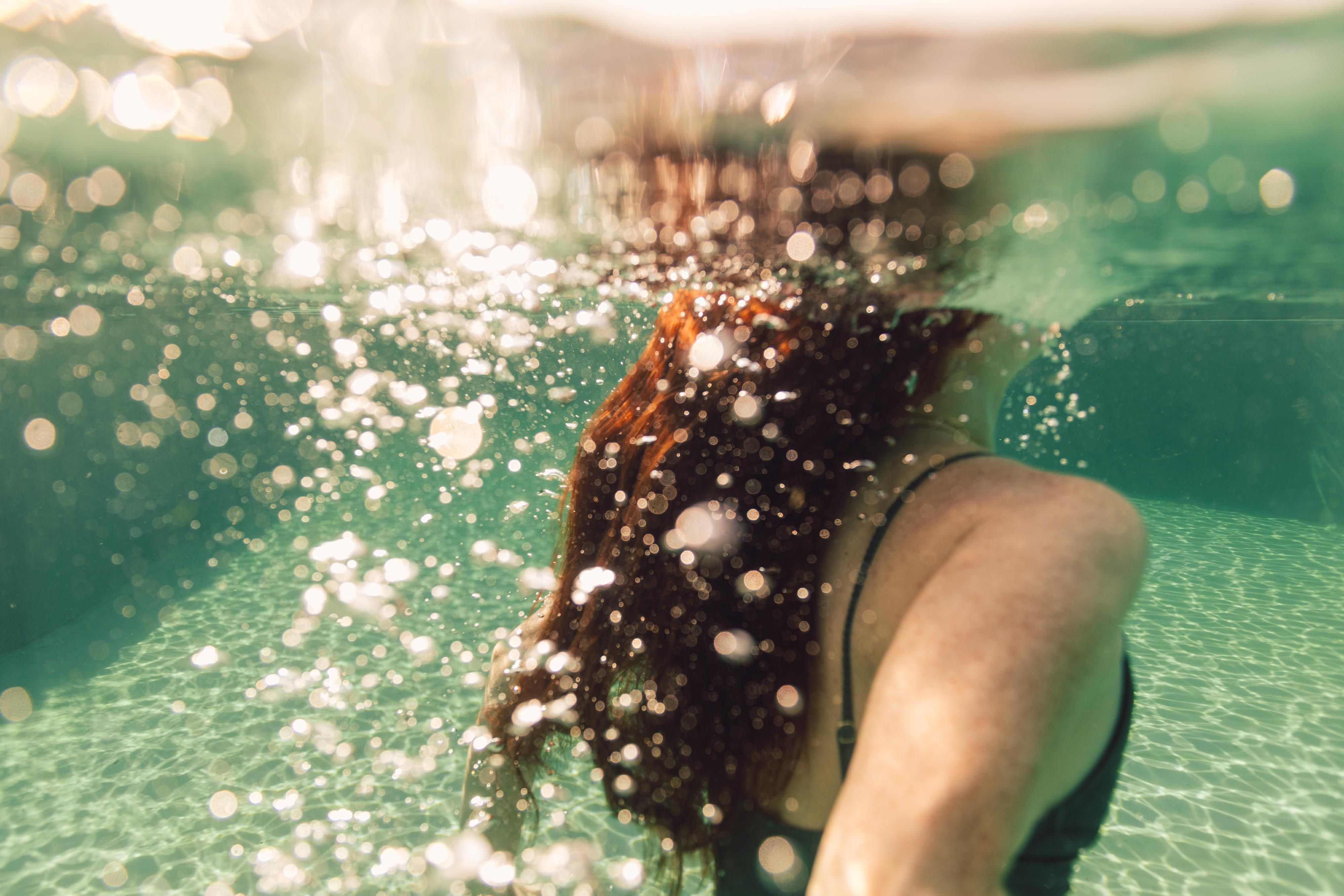 A person swims underwater, surrounded by air bubbles. The water has a clear green color.