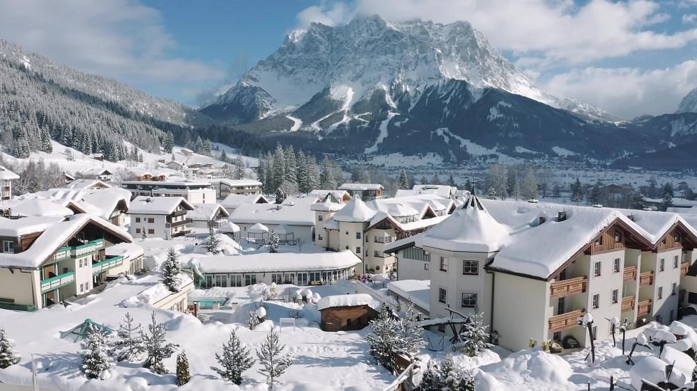 A picturesque winter landscape with snow-covered houses and mountains in the background. The clear blue sky complements the peaceful atmosphere.