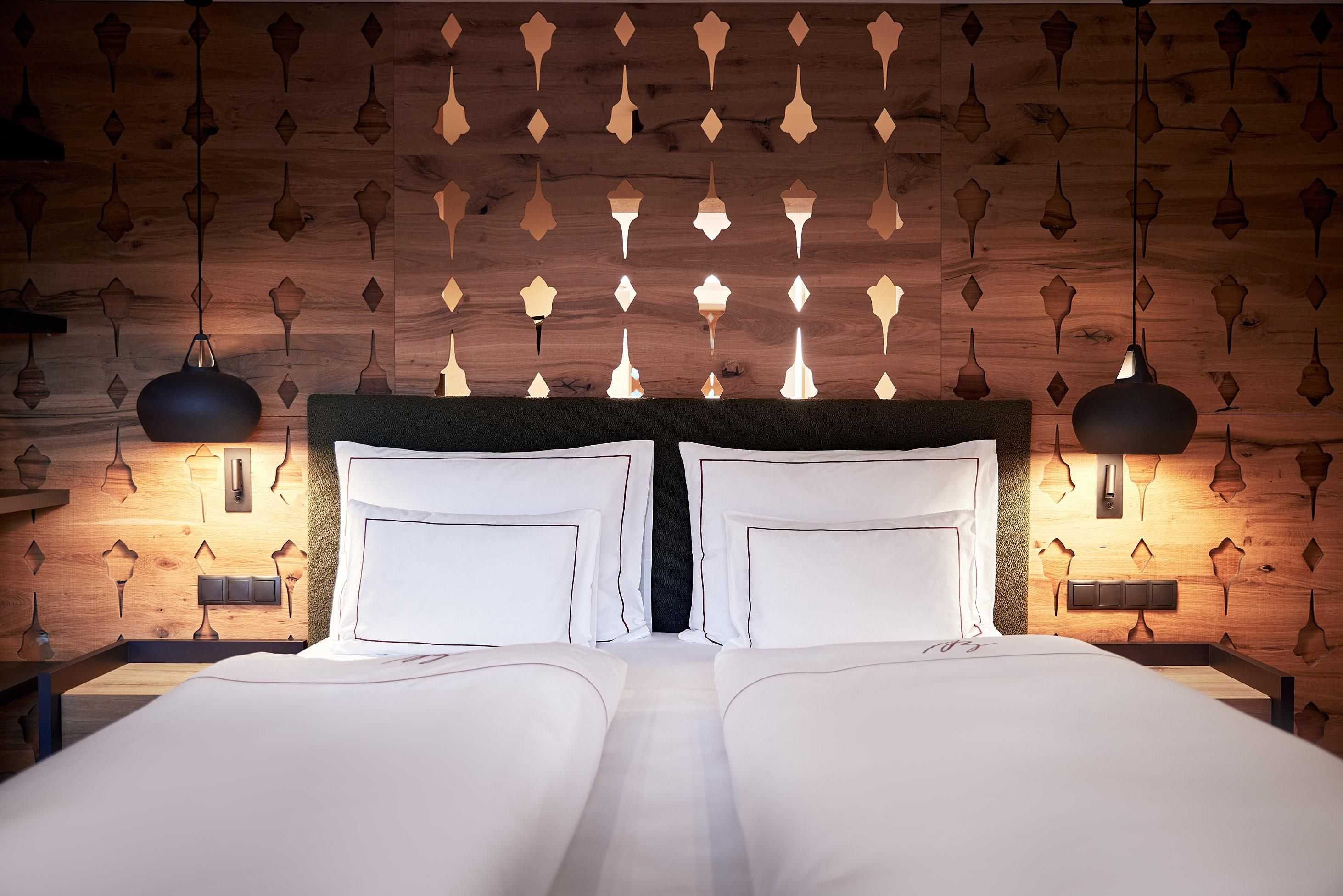 A modern bedroom with a double bed and elegant bed linens. The walls are made of wood with decorative elements and pleasant lighting.