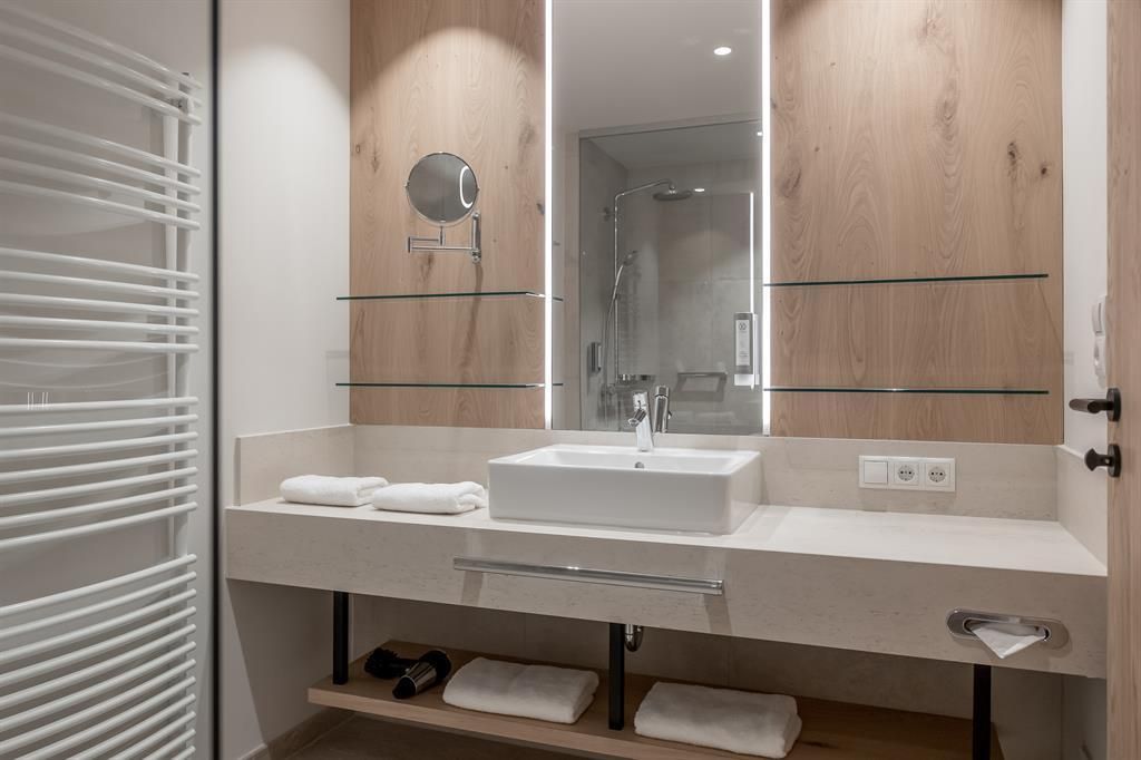 A modern bathroom with a sink and a large mirror. There are towels and a shower area with a glass wall.