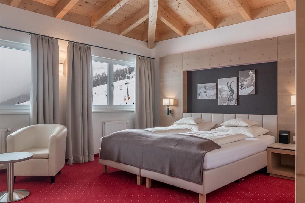 A modern hotel room with a large bed and a cozy armchair. Large windows provide a view of the snowy landscape.