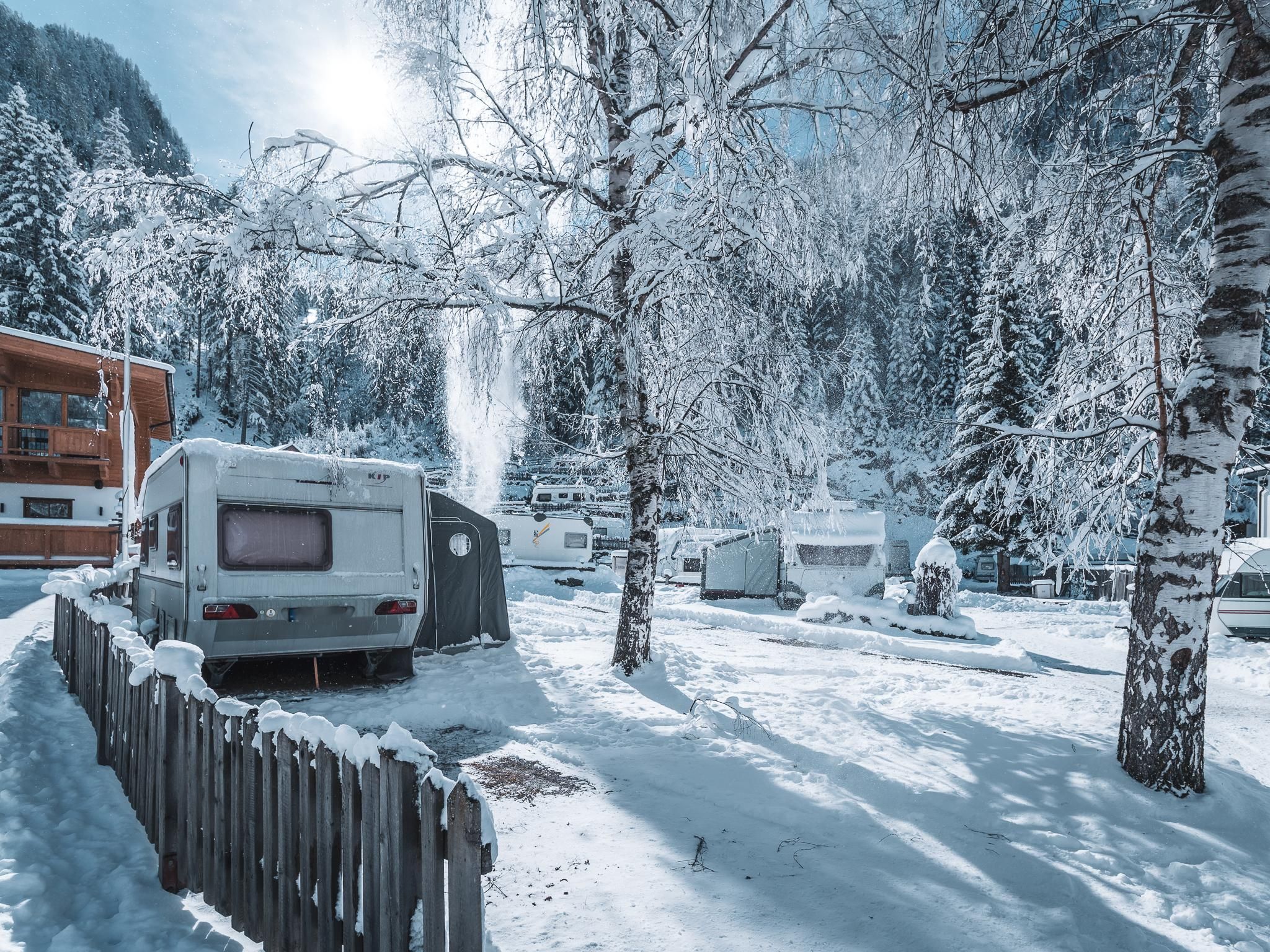 A winter campsite with caravans and snow-covered trees. The landscape is peaceful and characterized by a frosty glow.