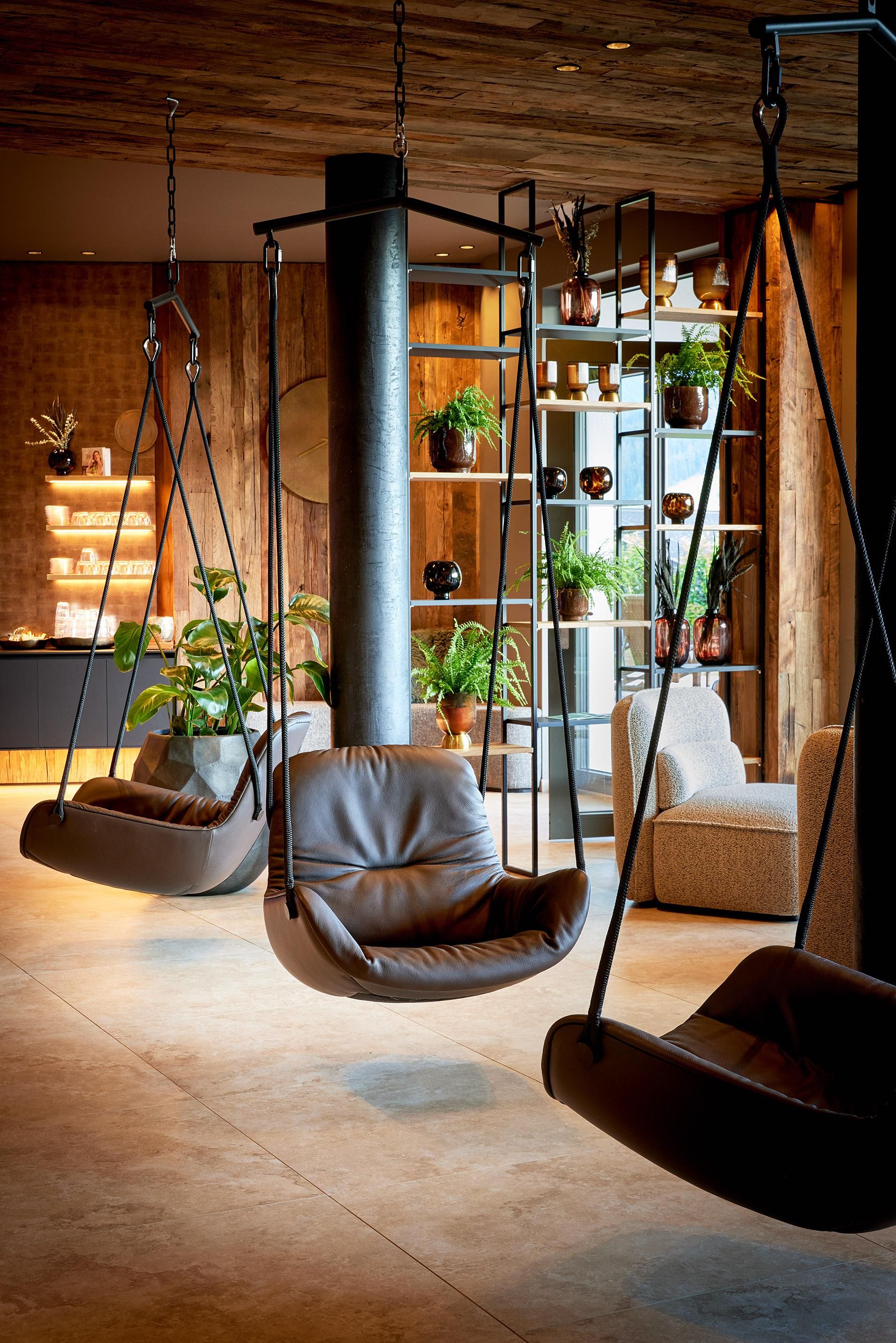 A modern interior view with swinging chairs and green plants. The room has a cozy and inviting atmosphere.