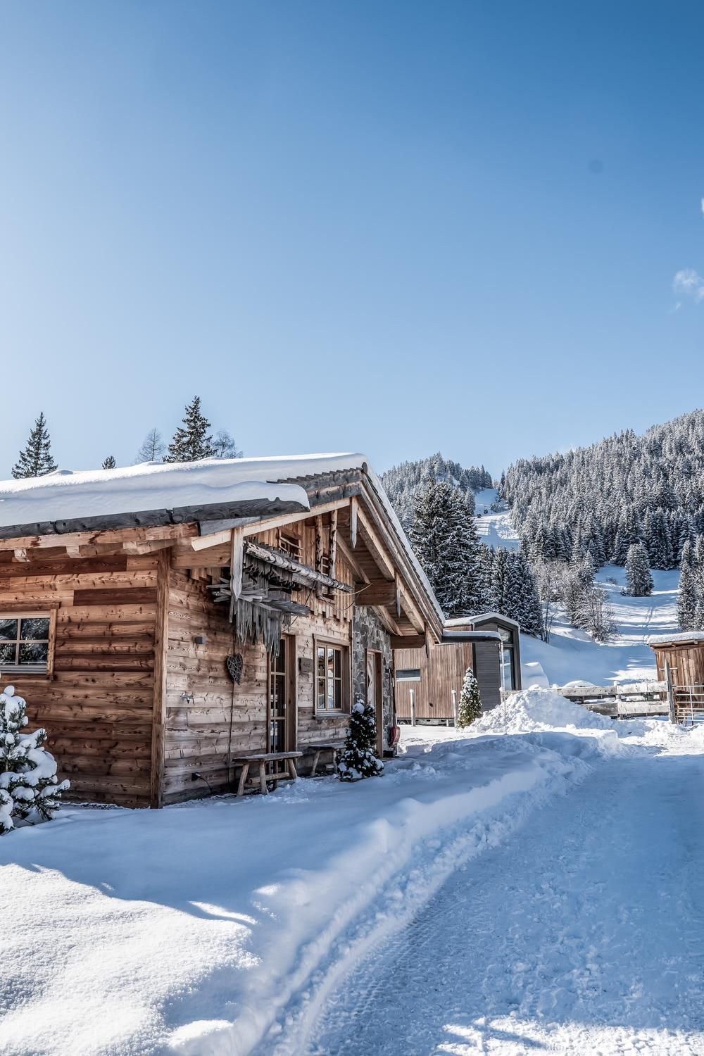A winter chalet in a snowy landscape. In the background, majestic mountains rise under a clear blue sky.