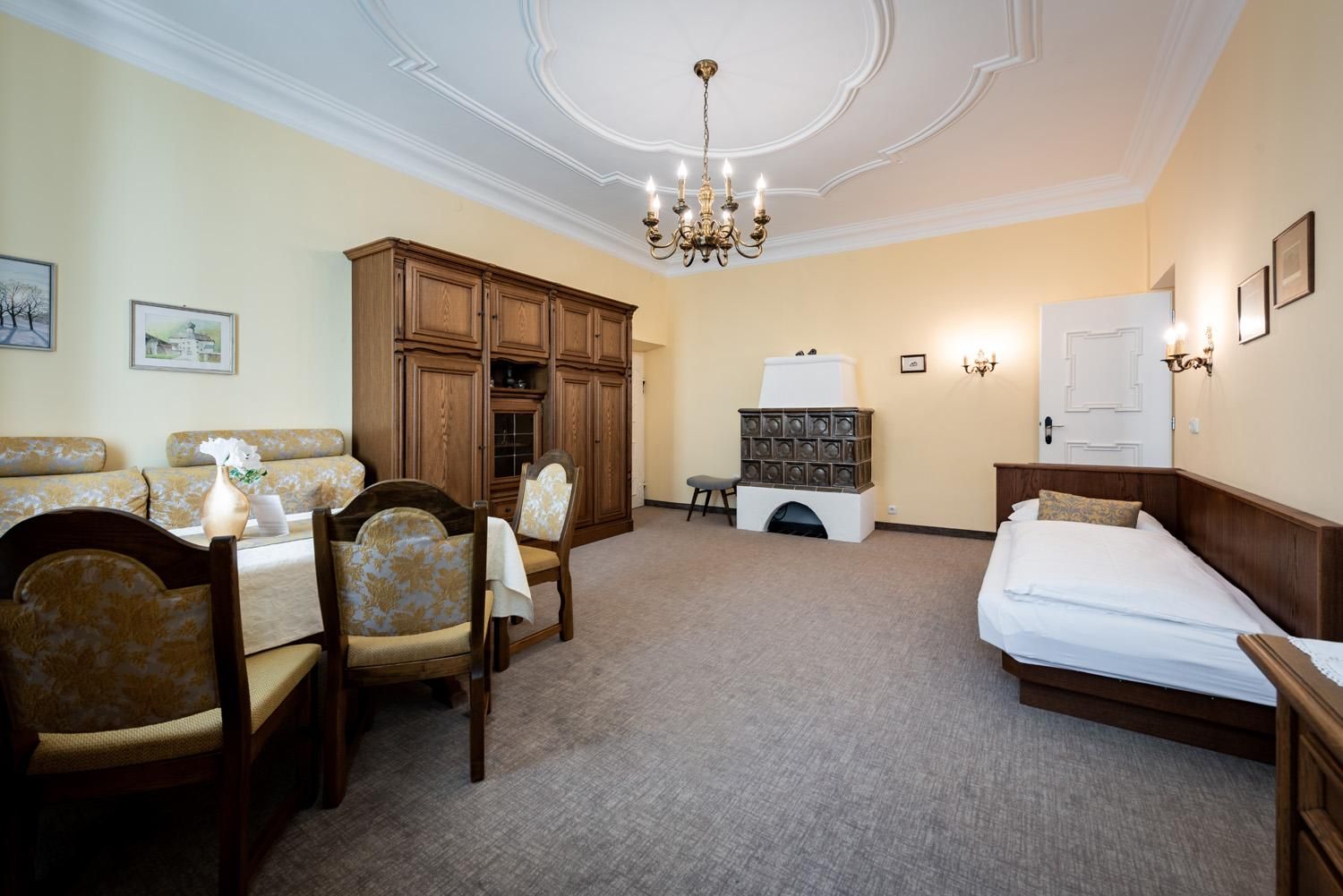 An inviting living space with wooden furniture and a large dining table. The walls are painted in soft yellow tones and the room features a historic stove.