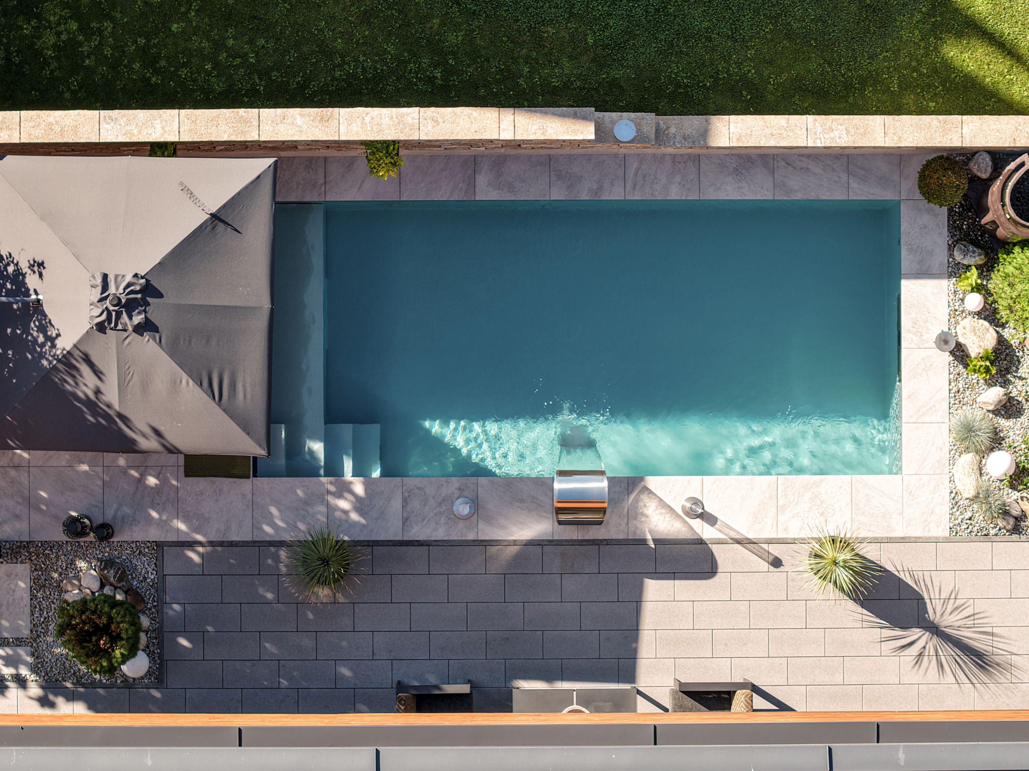 An elegant pool surrounded by a well-maintained garden. Sun umbrellas and plants create a relaxed atmosphere.