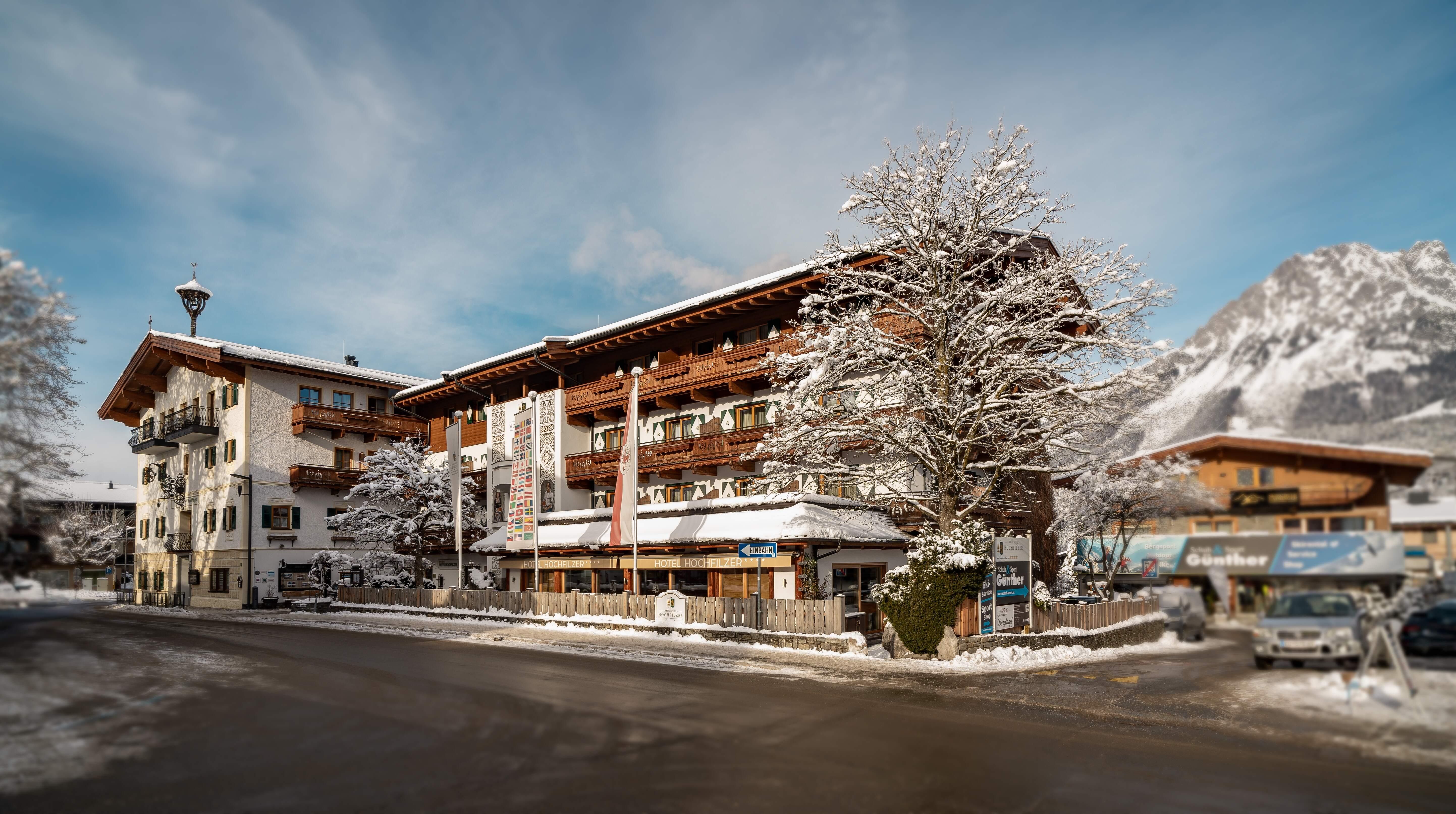 A picturesque building in a winter setting with snow-covered trees. In the background, mountains and a clear sky can be seen.