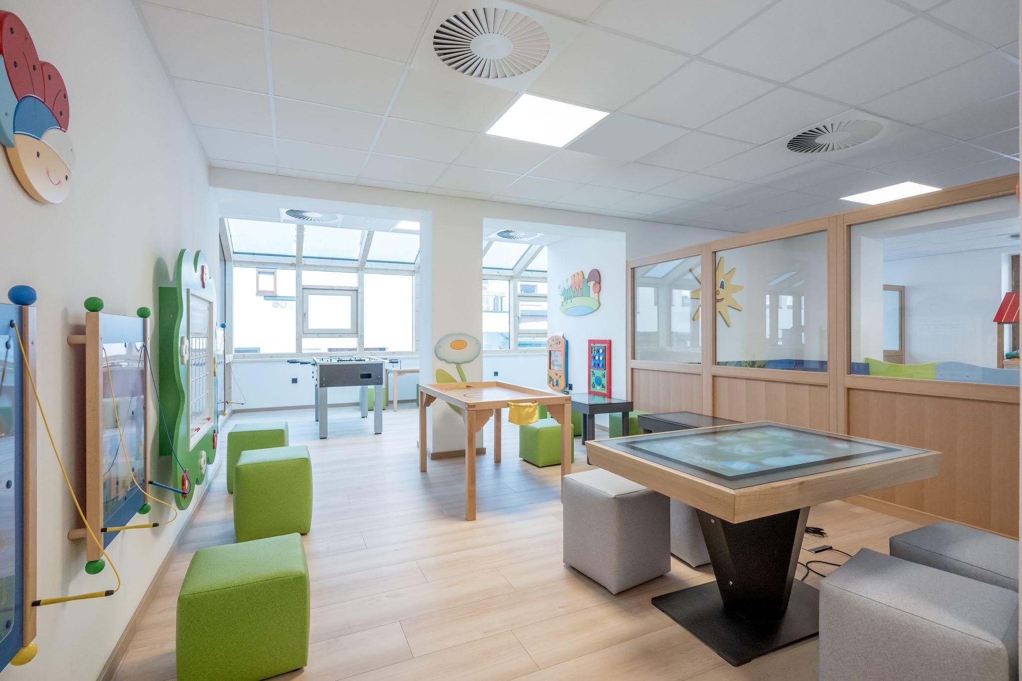 A bright and child-friendly room with multifunctional tables and colorful furniture. The walls are decorated with cheerful pictures, creating an inviting atmosphere.