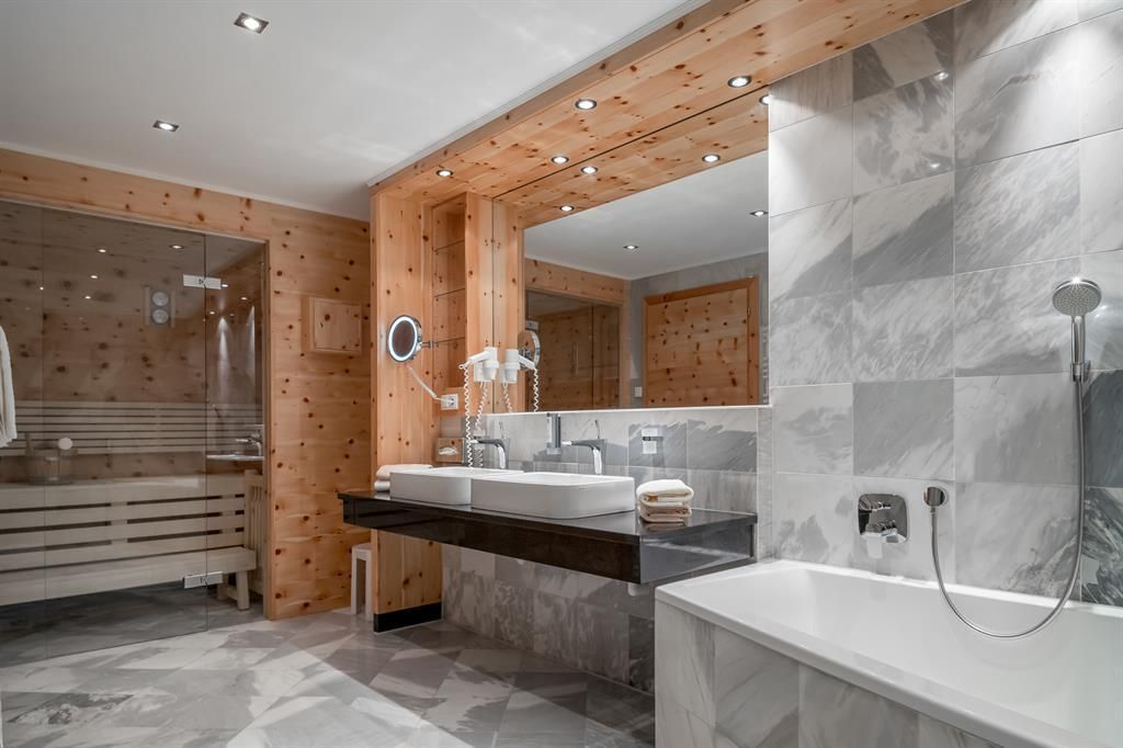 A modern bathroom with wooden walls and a large mirror. It features a shower, a bathtub, and a double sink.