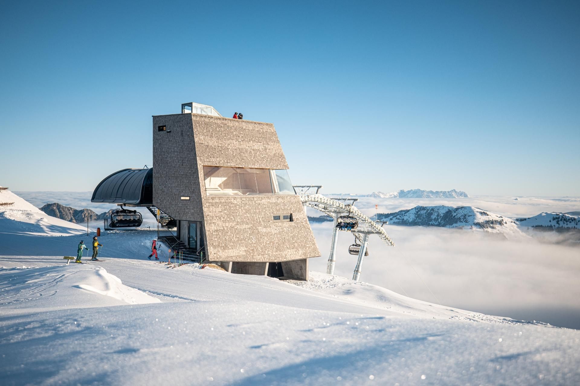 A modern building in the mountains, surrounded by snow-covered landscapes. In the background, the mountain peaks and a ski lift are visible.