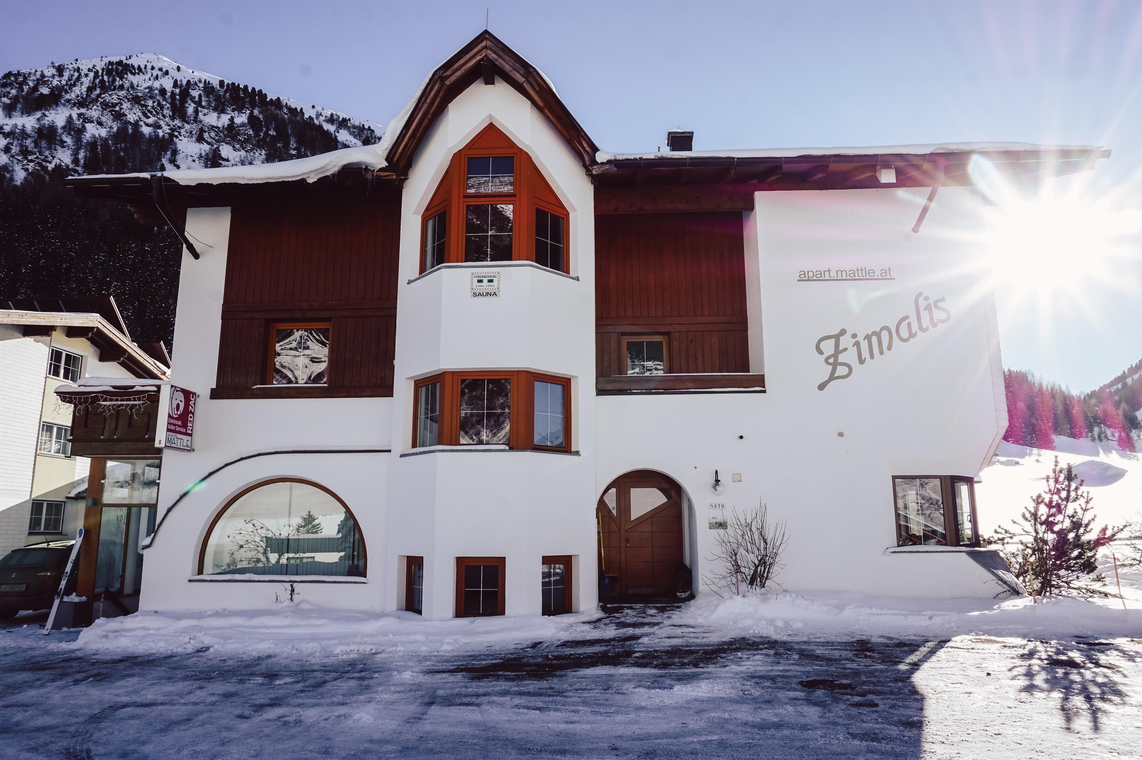 A charming building in alpine style, surrounded by snow. The sun shines on the facade, creating an inviting atmosphere.