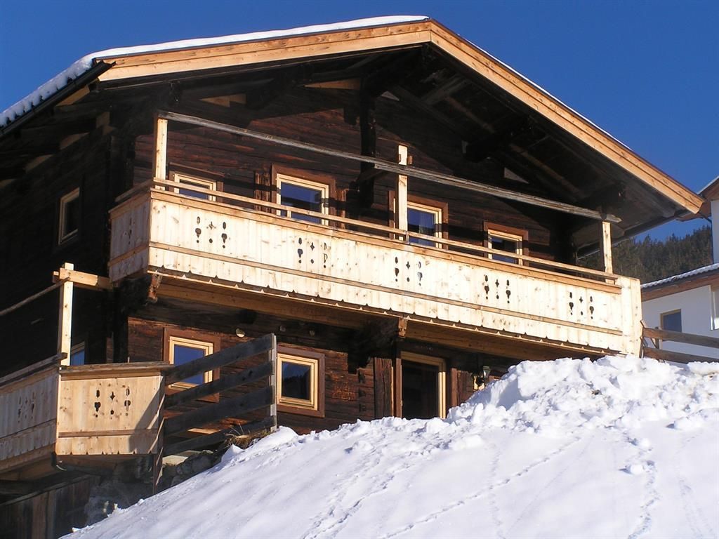 A charming wooden house with a balcony, surrounded by snow. The clear blue sky creates a wintry atmosphere.